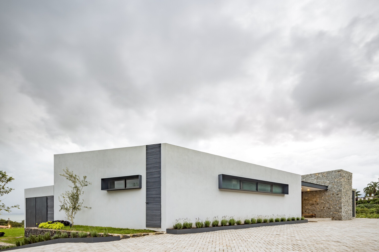 A textured stone wall guides visitors toward the entry, anchoring the home to its lakeside hillside setting.