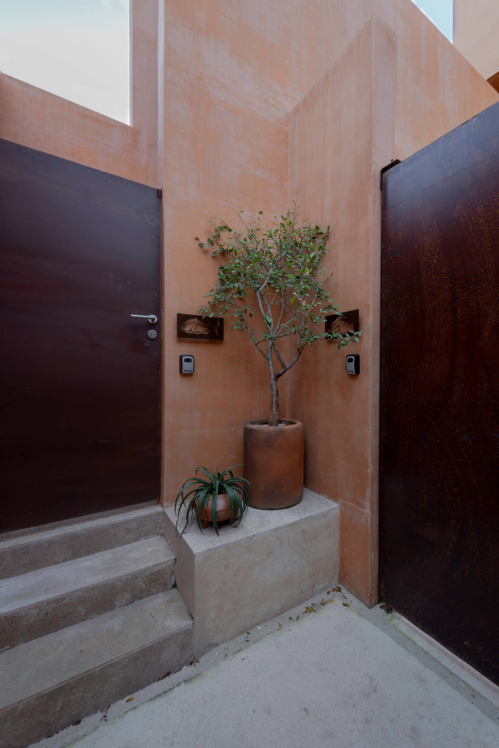 A narrow alley opens to a courtyard that becomes the home’s peaceful center, linking both living units and framing the transition from street to sanctuary.