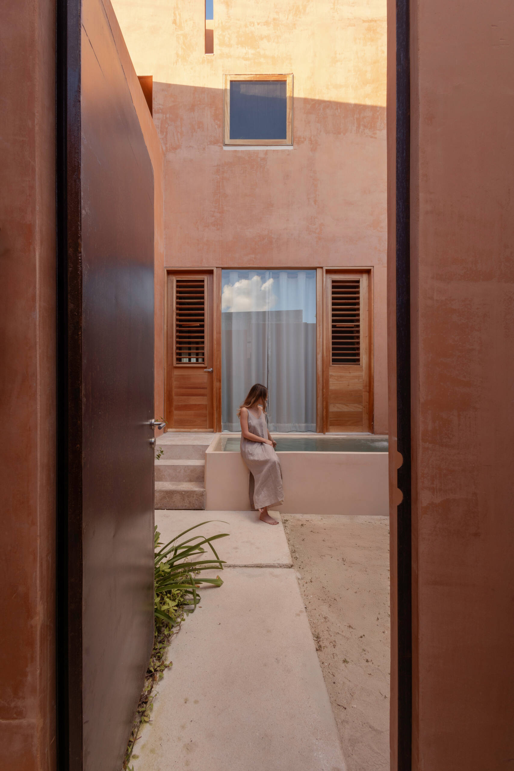 A narrow alley opens to a courtyard that becomes the home’s peaceful center, linking both living units and framing the transition from street to sanctuary.
