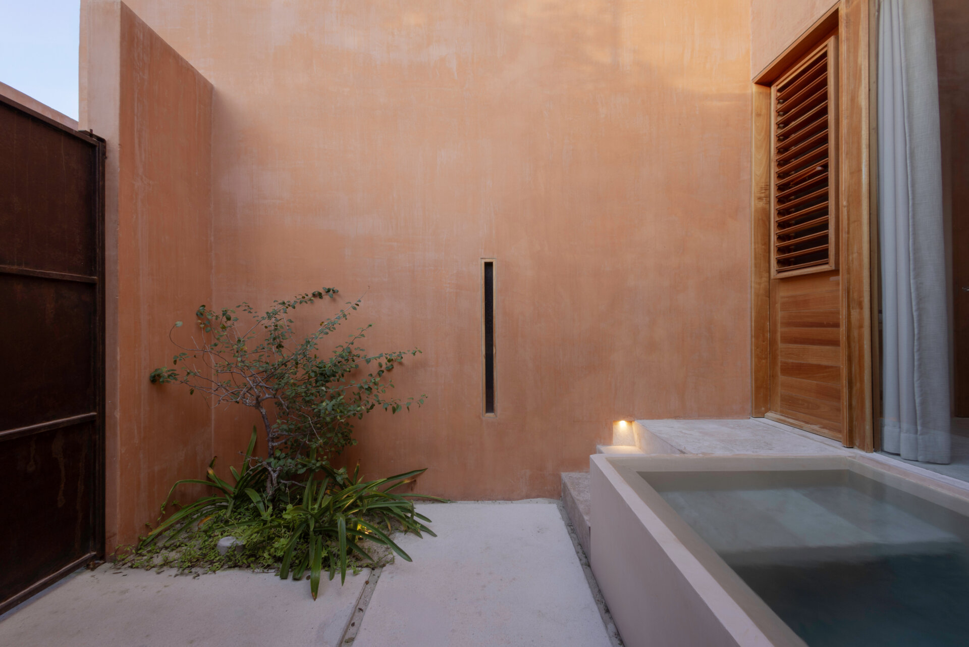 A narrow alley opens to a courtyard that becomes the home’s peaceful center, linking both living units and framing the transition from street to sanctuary.