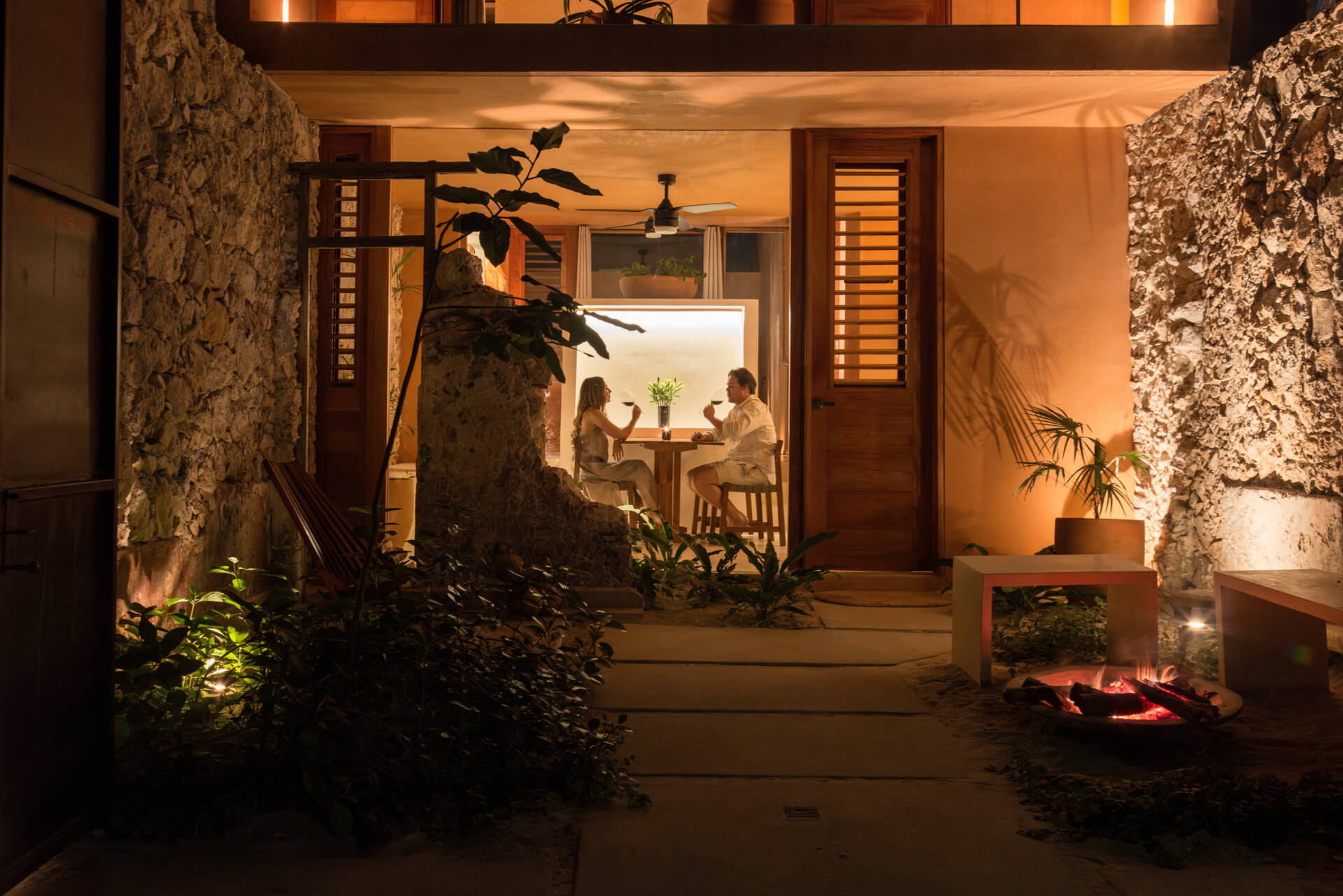 The lower unit features a garden, open kitchen, dining area, bedroom, and bathroom, designed to feel airy and connected through two sunlit courtyards.