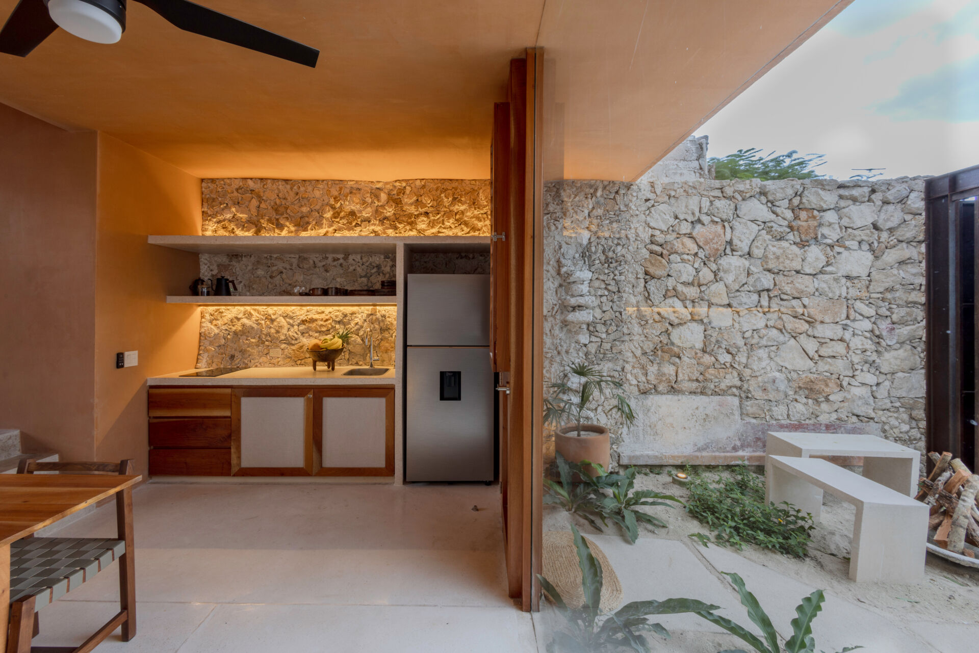 The lower unit features a garden, open kitchen, dining area, bedroom, and bathroom, designed to feel airy and connected through two sunlit courtyards.
