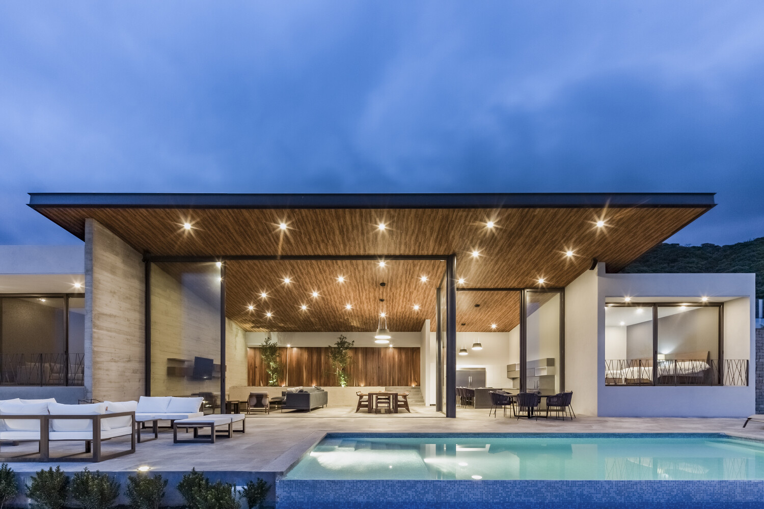 Sliding glass walls open to a pool, firepit, and shaded lounge, turning every day into lakeside living.