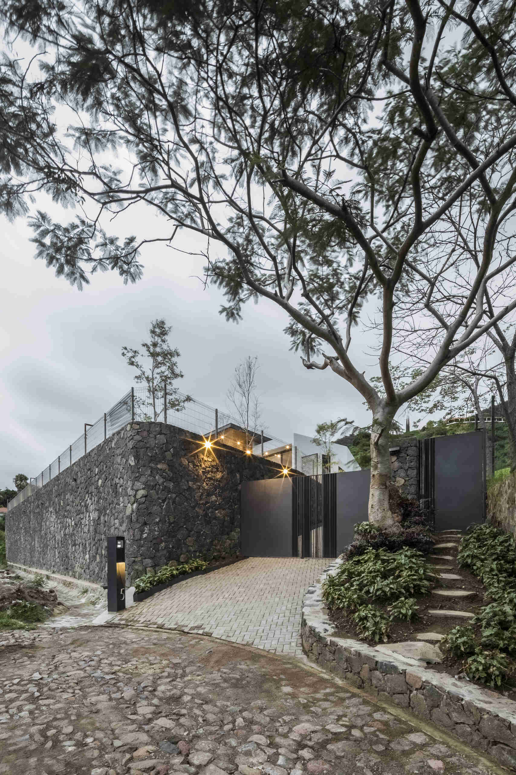 A textured stone wall guides visitors toward the entry, anchoring the home to its lakeside hillside setting.