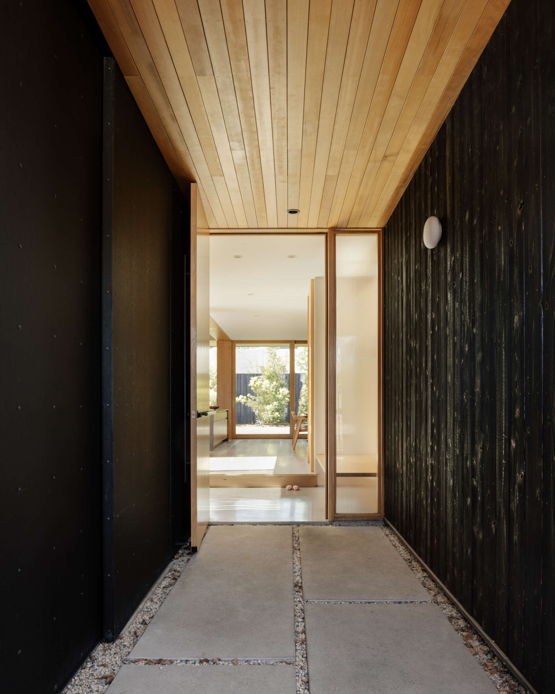 A slatted wood gate, partially hidden by concrete walls, marks the entrance through a small courtyard. This leads to the “genkan,” a recessed transitional space for removing shoes. The entry sets the tone for a home designed to merge practicality with moments of discovery.