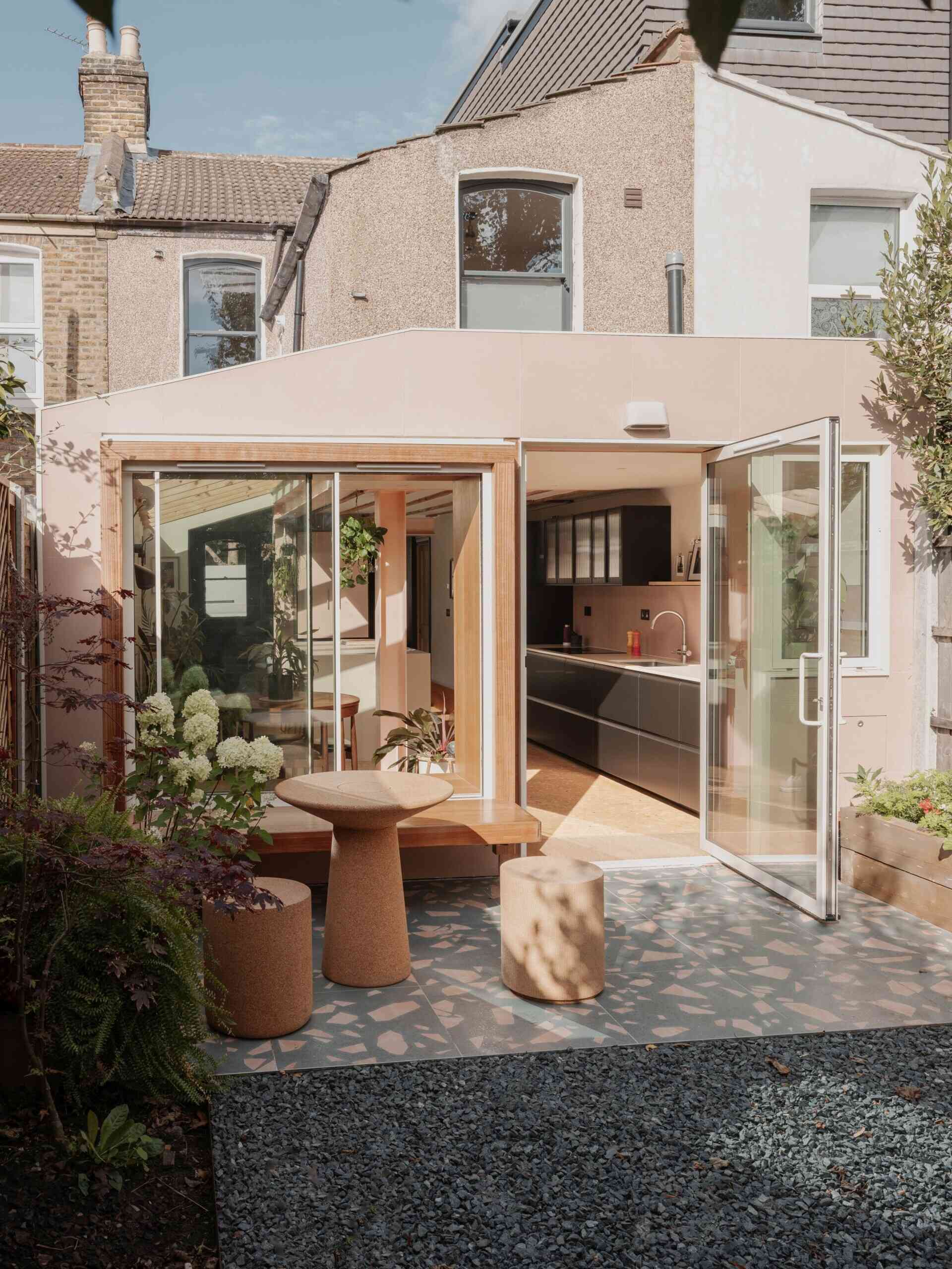 A light-filled garden extension with a new kitchen and dining area, includes pink steel, cork flooring, a pivoting door, and rooflights.