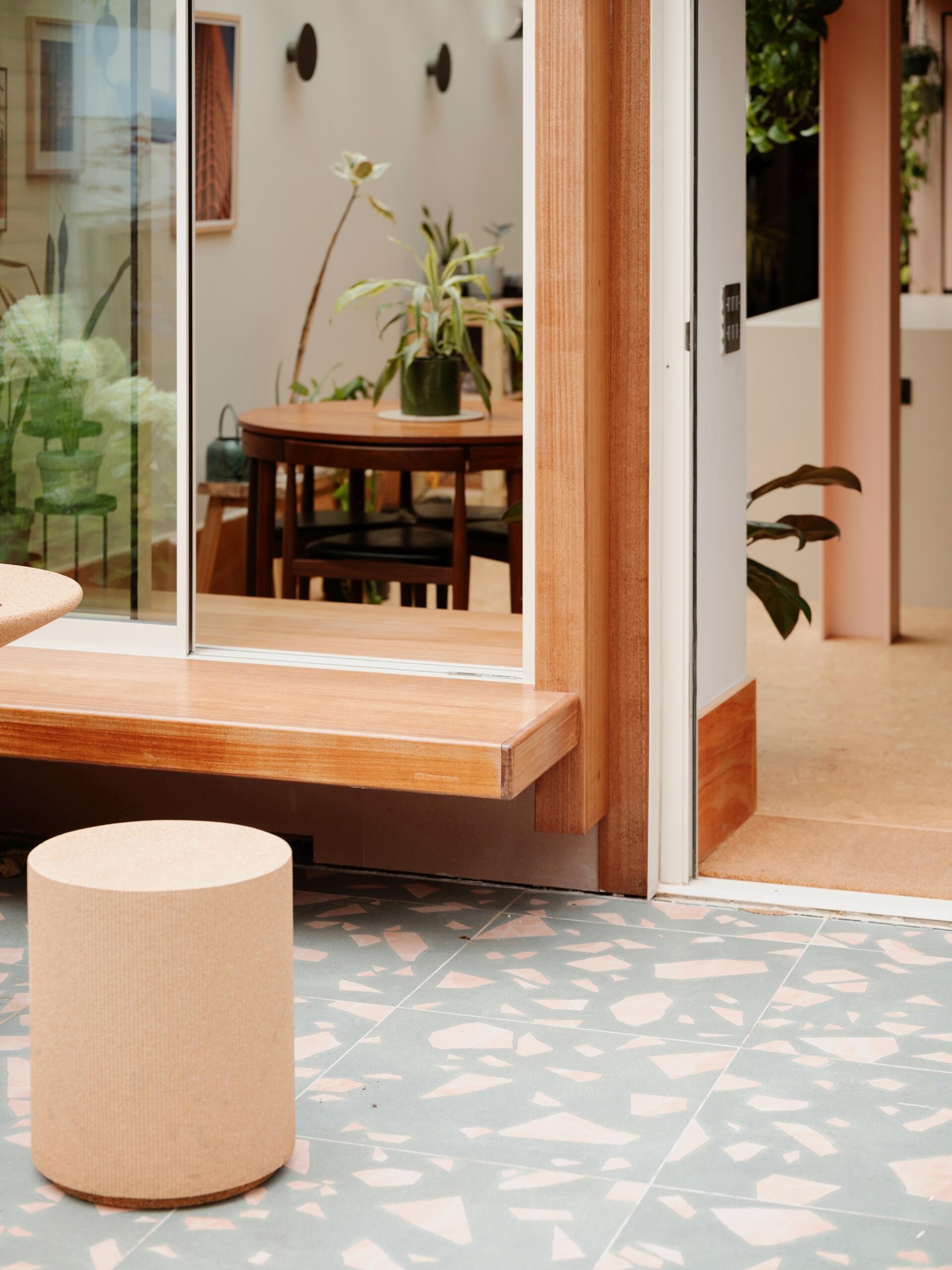 A light-filled garden extension with a new kitchen and dining area, includes pink steel, cork flooring, a pivoting door, and rooflights.