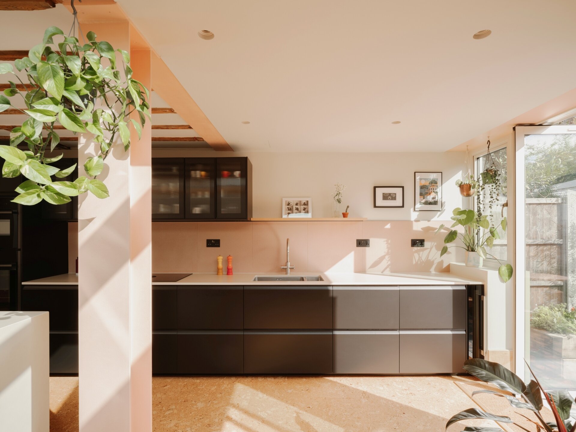 A light-filled garden extension with a new kitchen and dining area, includes pink steel, cork flooring, a pivoting door, and rooflights.