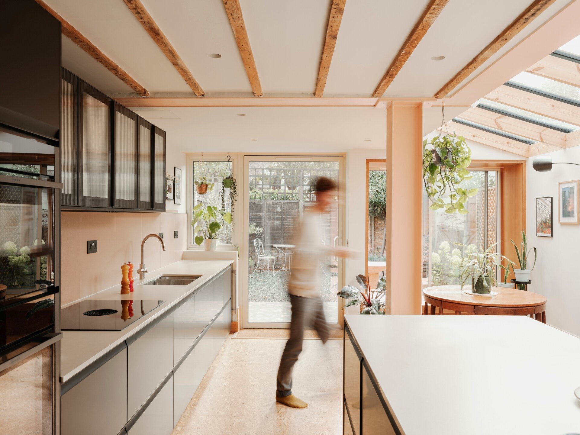 A light-filled garden extension with a new kitchen and dining area, includes pink steel, cork flooring, a pivoting door, and rooflights.