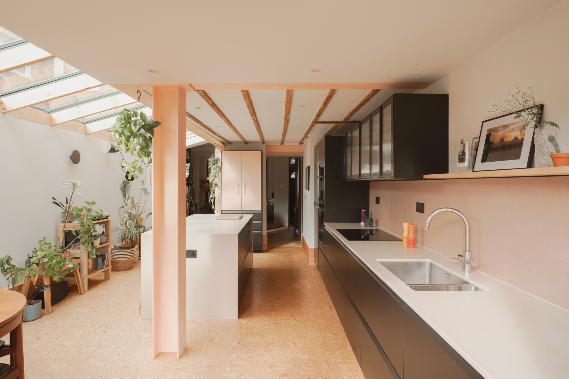 A light-filled garden extension with a new kitchen and dining area, includes pink steel, cork flooring, a pivoting door, and rooflights.