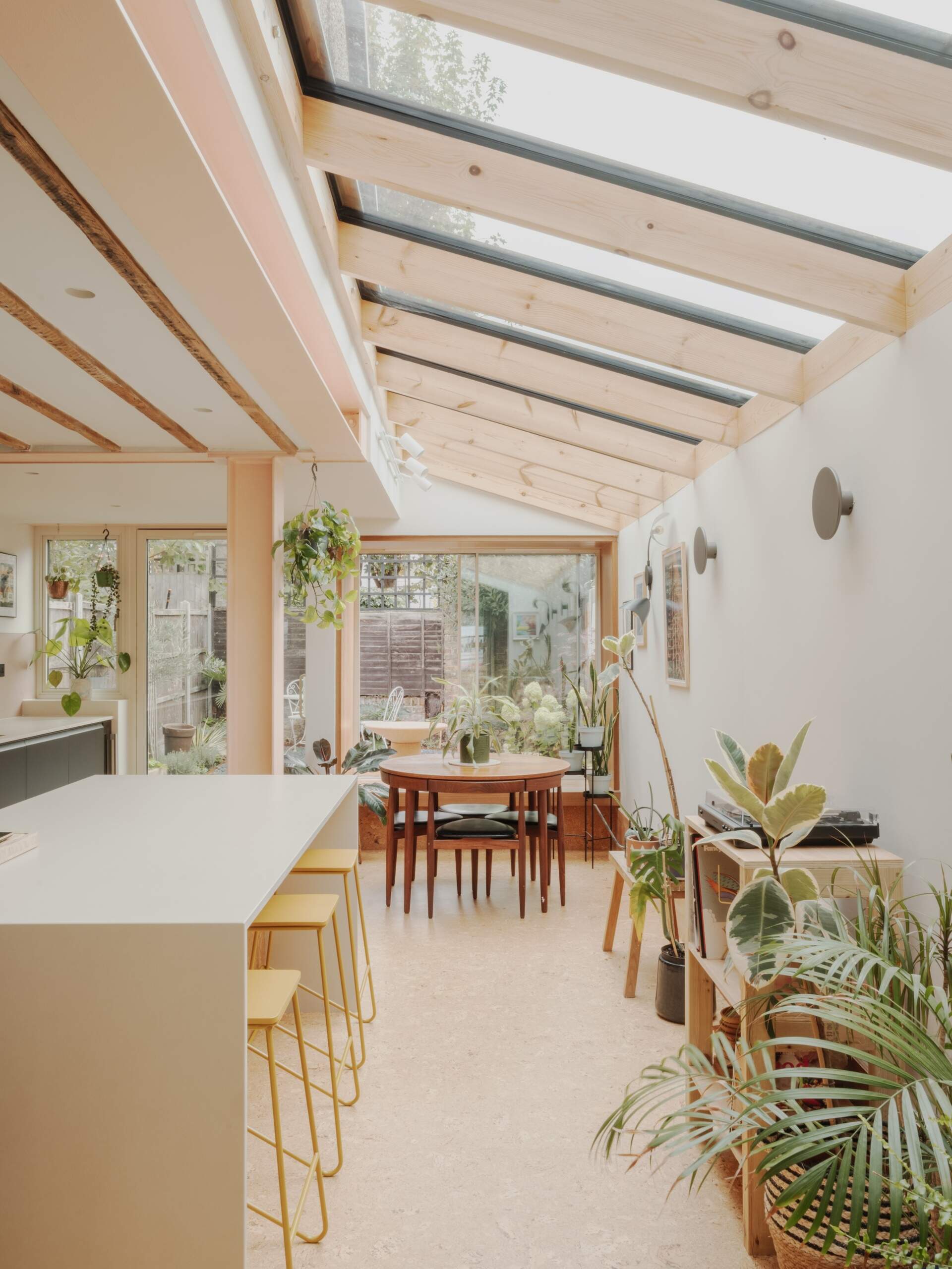 A light-filled garden extension with a new kitchen and dining area, includes pink steel, cork flooring, a pivoting door, and rooflights.