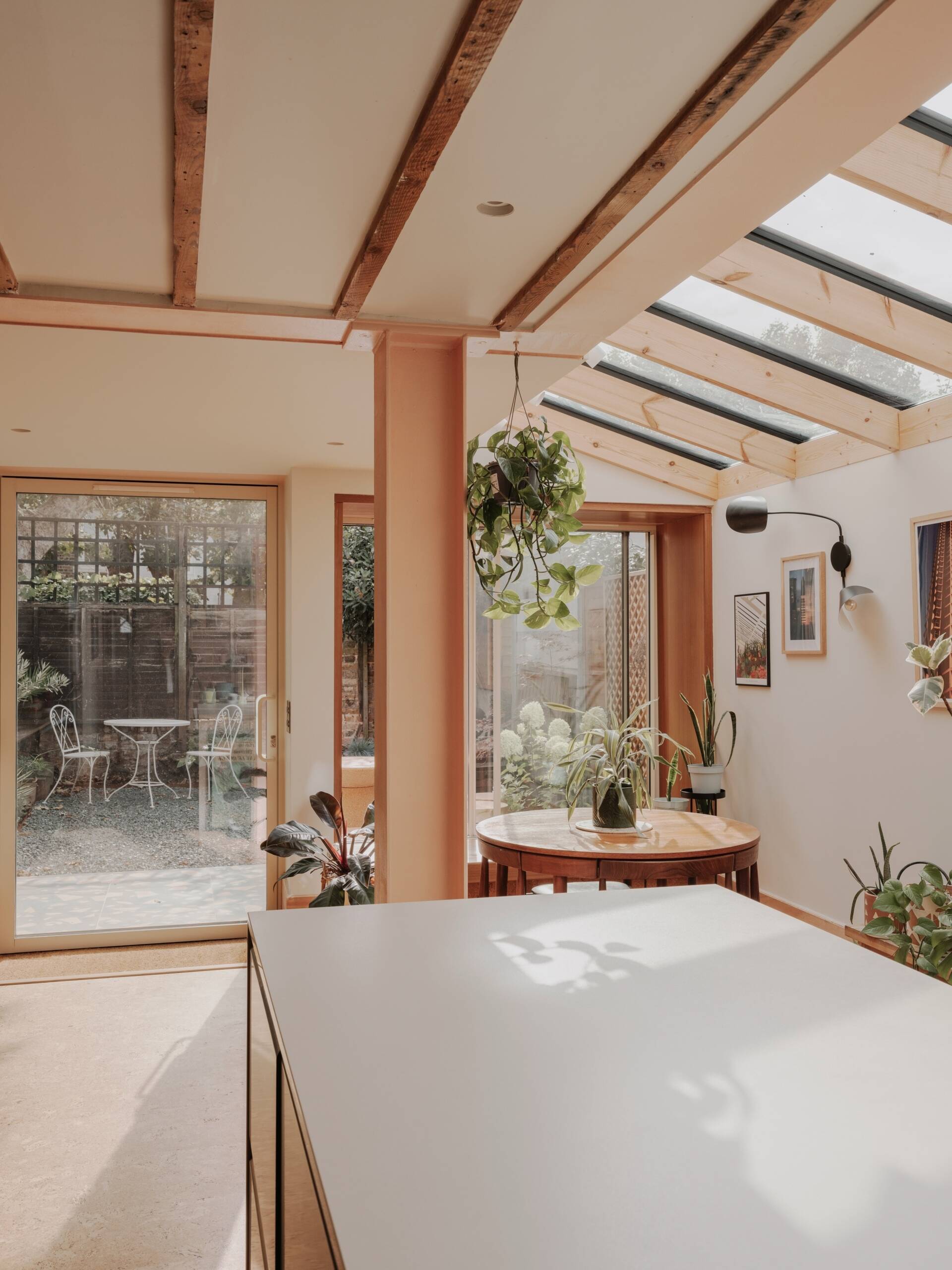 A light-filled garden extension with a new kitchen and dining area, includes pink steel, cork flooring, a pivoting door, and rooflights.