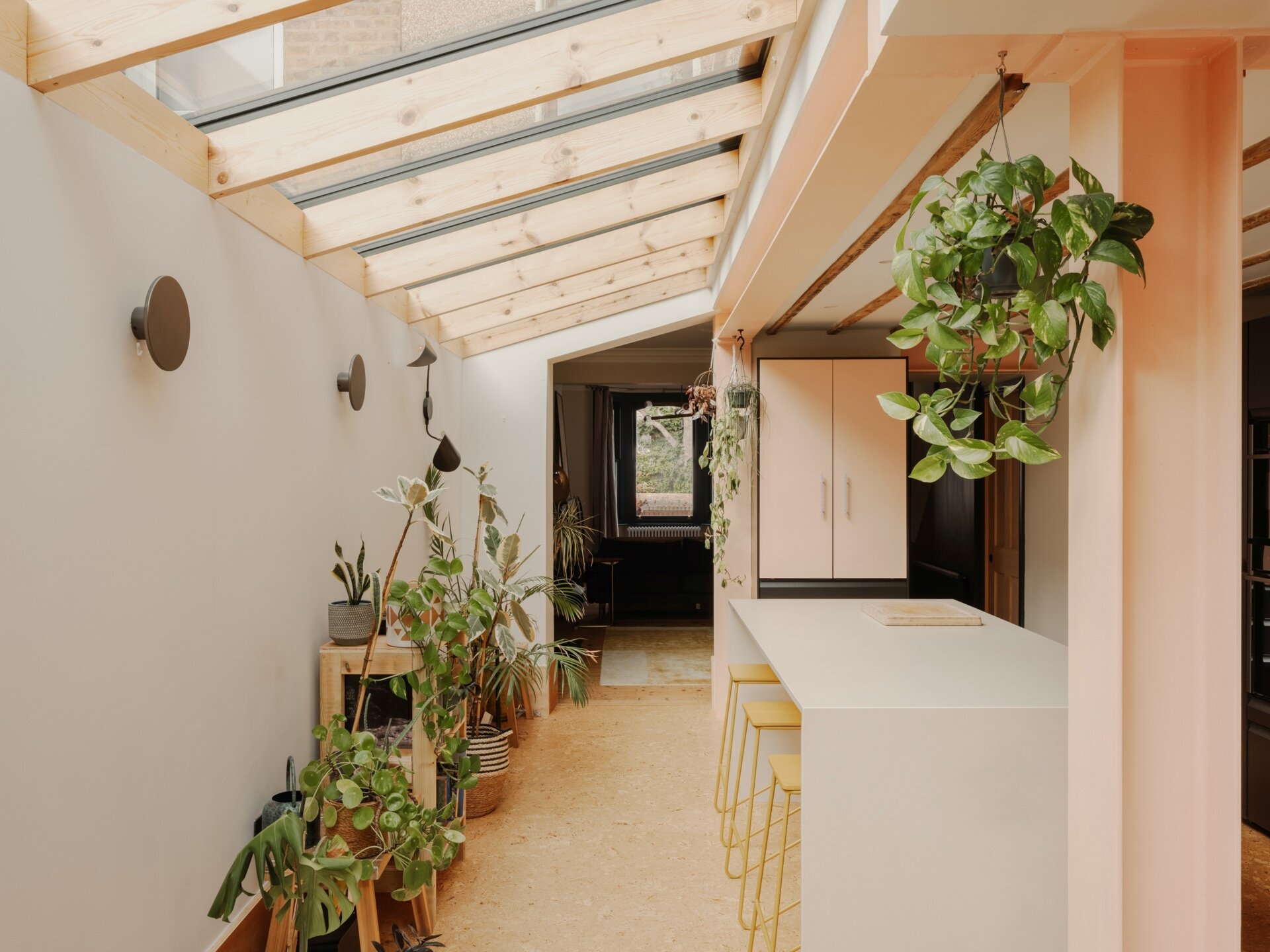 A light-filled garden extension with a new kitchen and dining area, includes pink steel, cork flooring, a pivoting door, and rooflights.