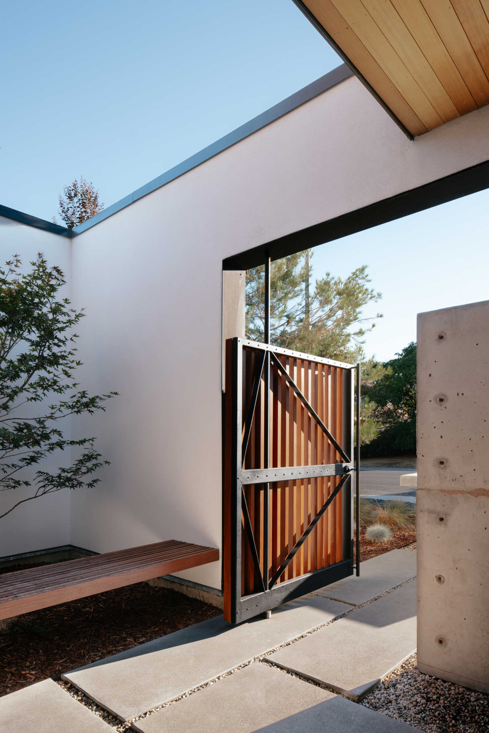 A slatted wood gate, partially hidden by concrete walls, marks the entrance through a small courtyard. This leads to the “genkan,” a recessed transitional space for removing shoes. The entry sets the tone for a home designed to merge practicality with moments of discovery.