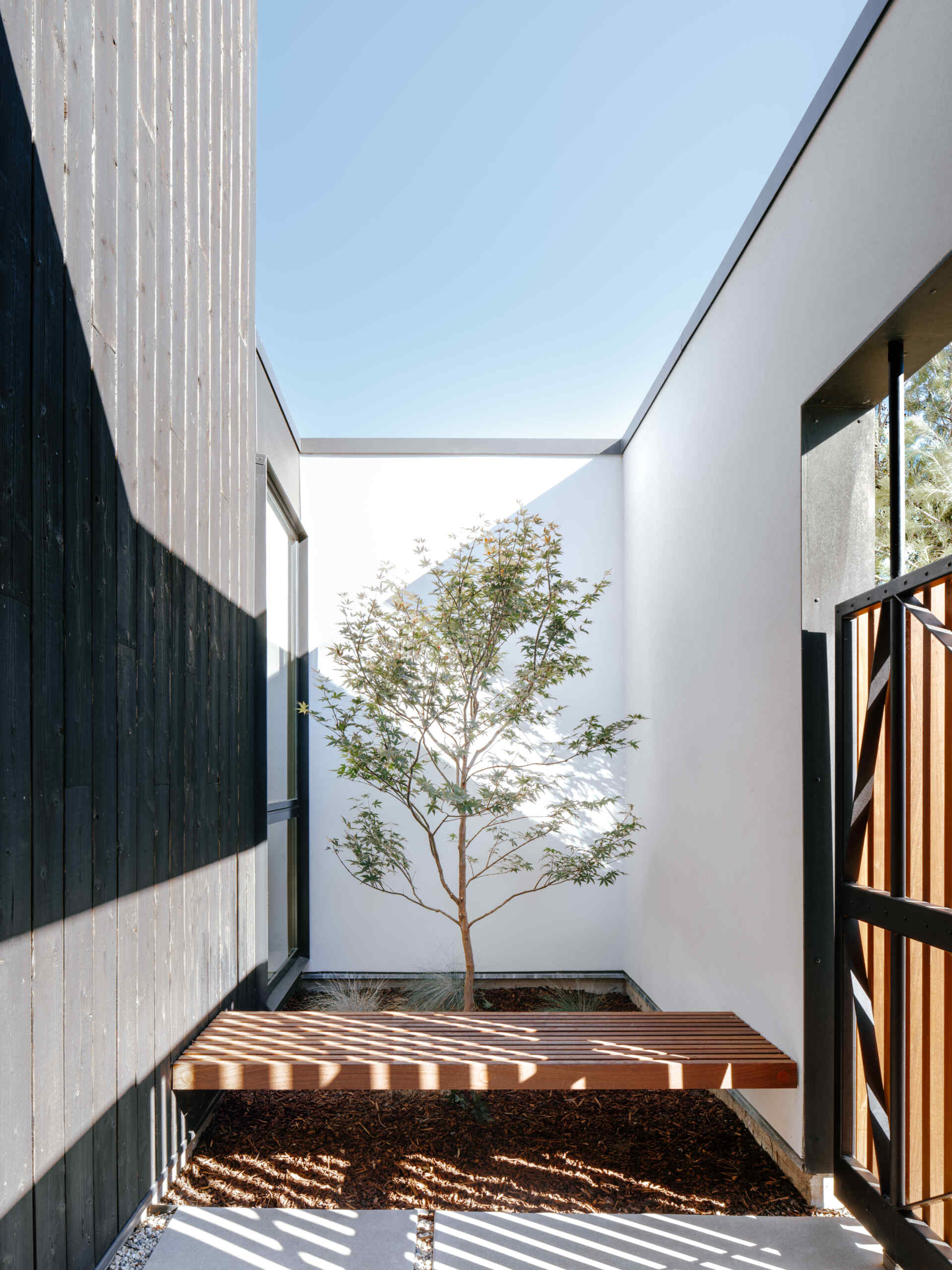 A slatted wood gate, partially hidden by concrete walls, marks the entrance through a small courtyard. This leads to the “genkan,” a recessed transitional space for removing shoes. The entry sets the tone for a home designed to merge practicality with moments of discovery.