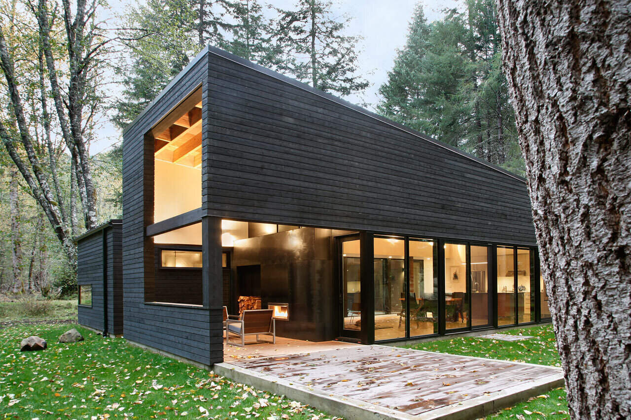 A covered outdoor living space with a fireplace connects the house to the river views beyond, perfect for cozy evenings in the woods.