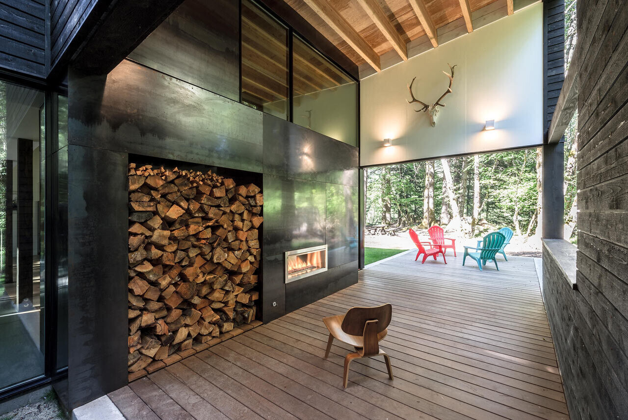A covered outdoor living space with a fireplace connects the house to the river views beyond, perfect for cozy evenings in the woods.