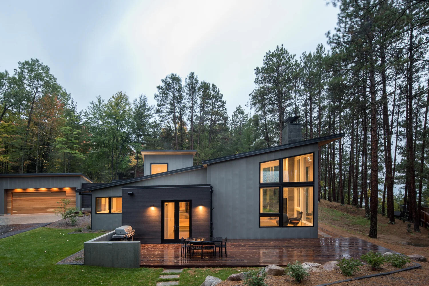 This modern house has a subtle dark exterior that includes grey, black, stone and wood elements, allowing the home to blend into the forested landscape.