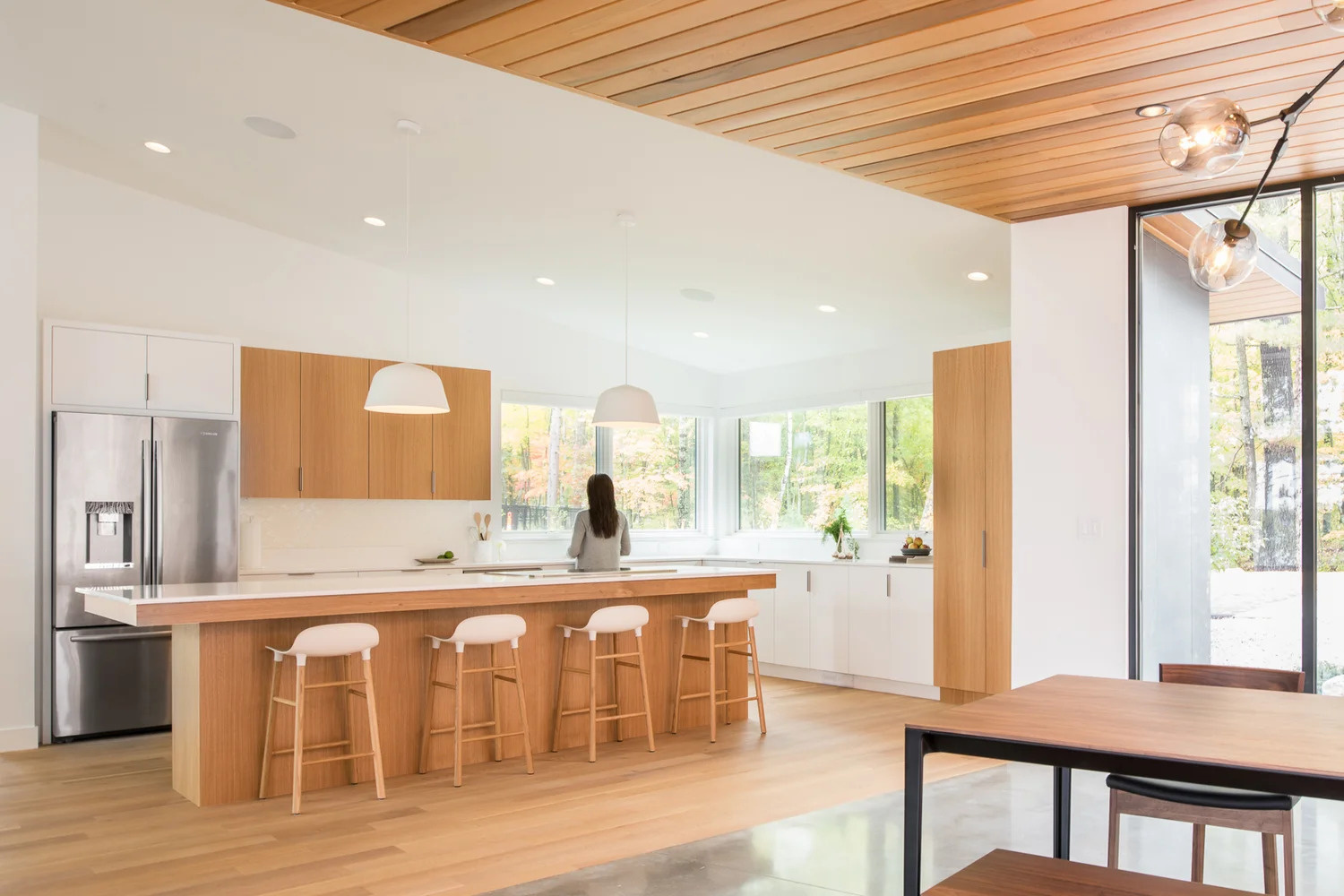 In this modern kitchen, bright white walls are warmed up with the use of white oak cabinets, and large windows let the surrounding tree views become the highlight of the kitchen.