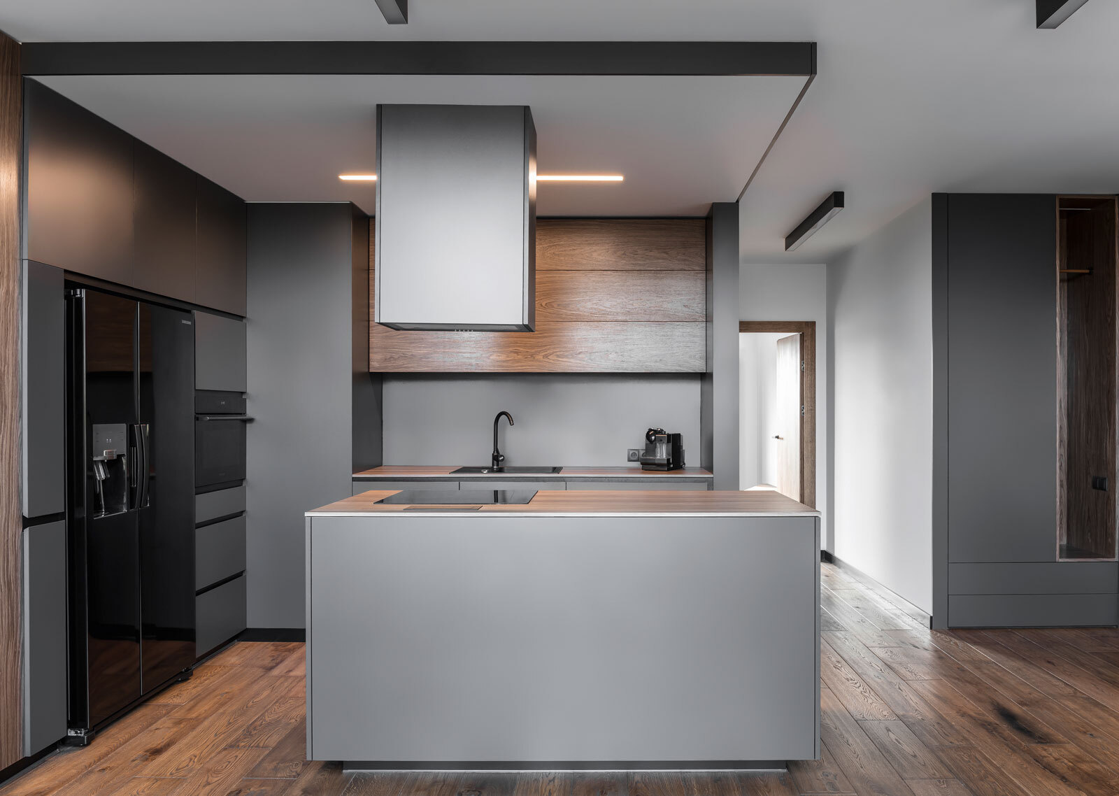 In this kitchen, dark grey walls and cabinets are softened by warm wood details. Glossy black appliances add a sleek, modern edge that complements the apartment’s masculine aesthetic. The minimalist palette continues through every surface, proving that simplicity can be expressive.