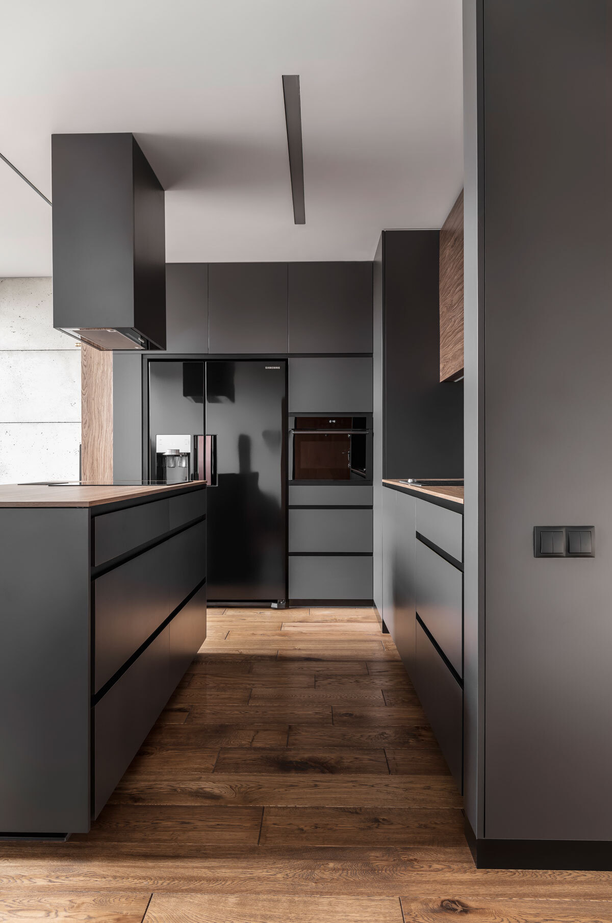 In this kitchen, dark grey walls and cabinets are softened by warm wood details. Glossy black appliances add a sleek, modern edge that complements the apartment’s masculine aesthetic. The minimalist palette continues through every surface, proving that simplicity can be expressive.