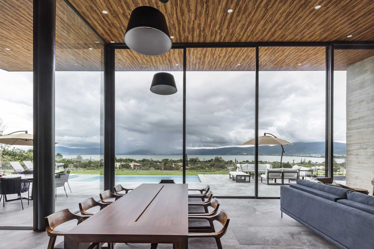 Sliding glass walls open to a pool, firepit, and shaded lounge, turning every day into lakeside living.