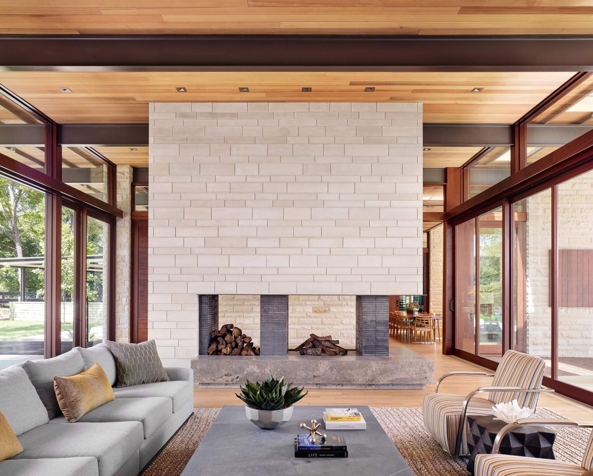 A stone fireplace anchors the main living space, framed by floor-to-ceiling windows that capture serene views of the front and back gardens.