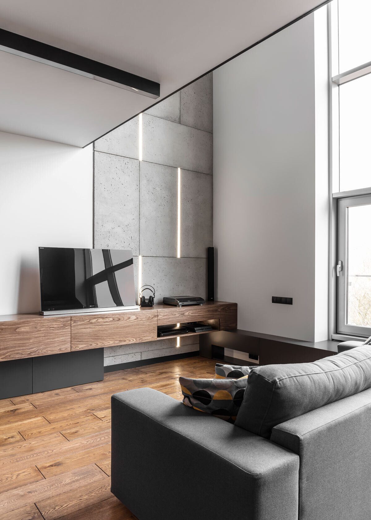 The living room features a concrete accent wall with embedded lighting and a custom wood console, blending warmth and minimalism in this modern apartment interior.