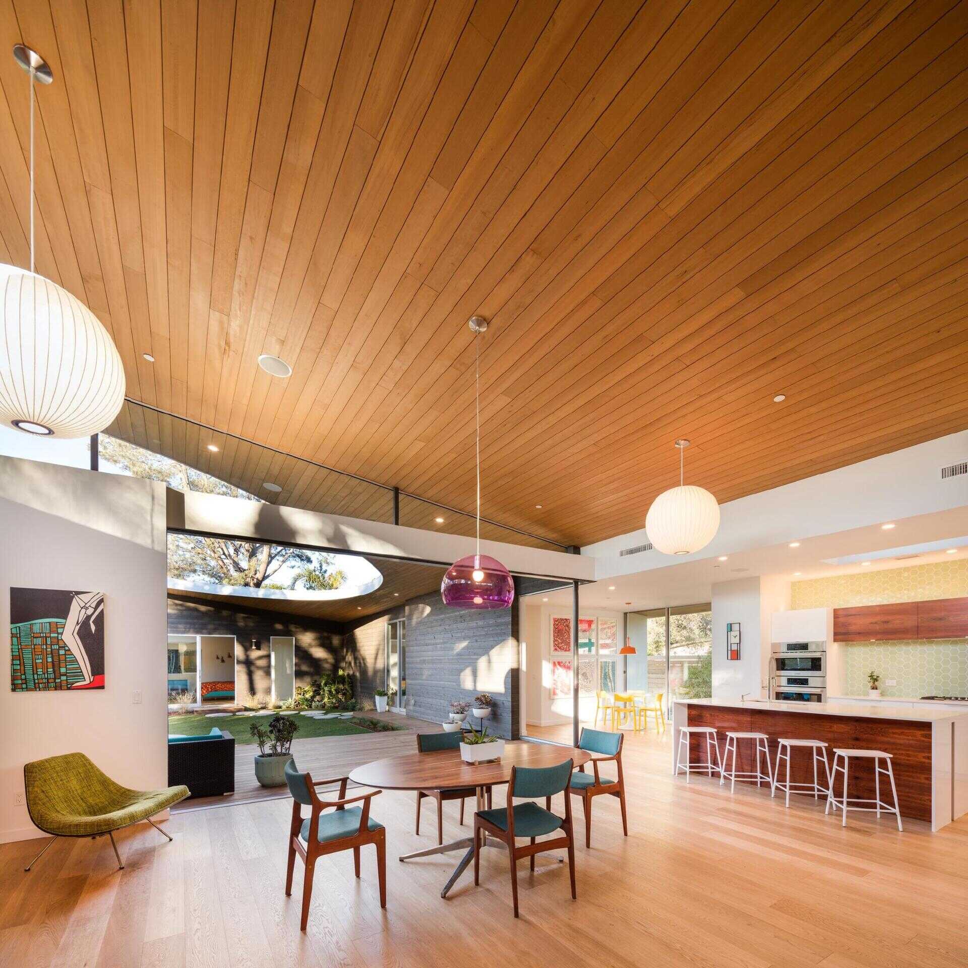 A purple pendant lamp and blue chairs bring playful color to a warm wood dining space.