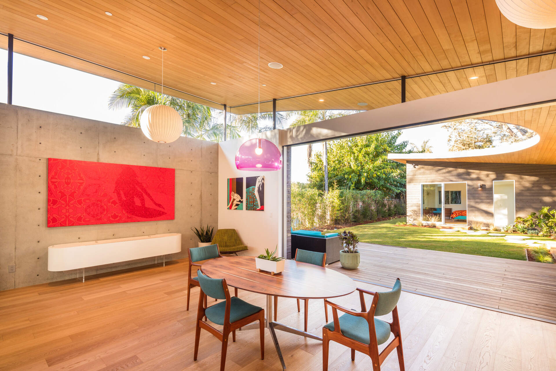 A purple pendant lamp and blue chairs bring playful color to a warm wood dining space.
