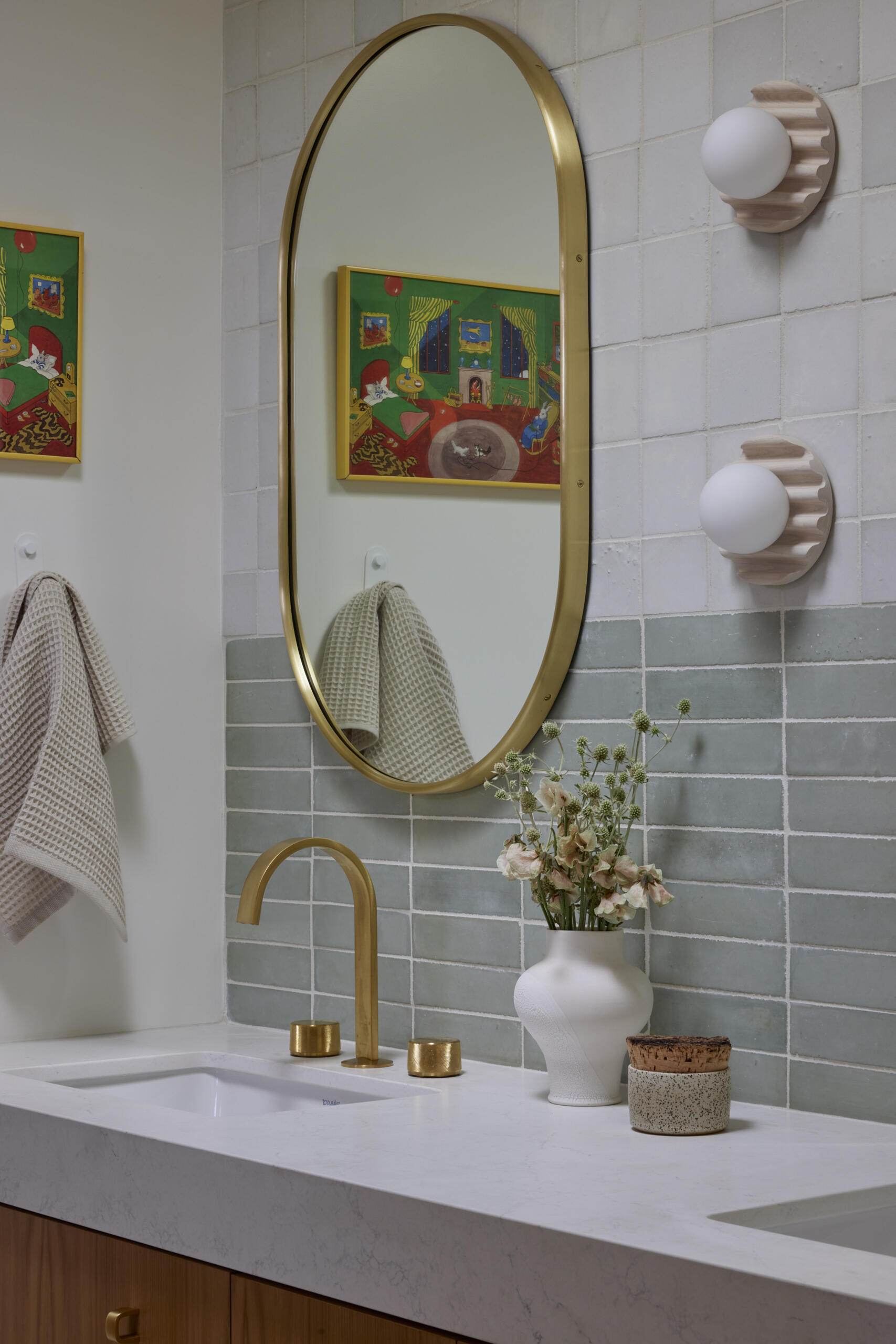 The kids bathroom strikes a balance between playful and practical. Terrazzo flooring provides a durable, easy-to-clean foundation, while soft green wall tiles add a calming touch. A wide vanity with wood drawers and brass hardware offers plenty of storage, designed to grow with the family. Rounded details, like the oval mirror, soften the clean lines, making the space inviting without losing its modern edge.