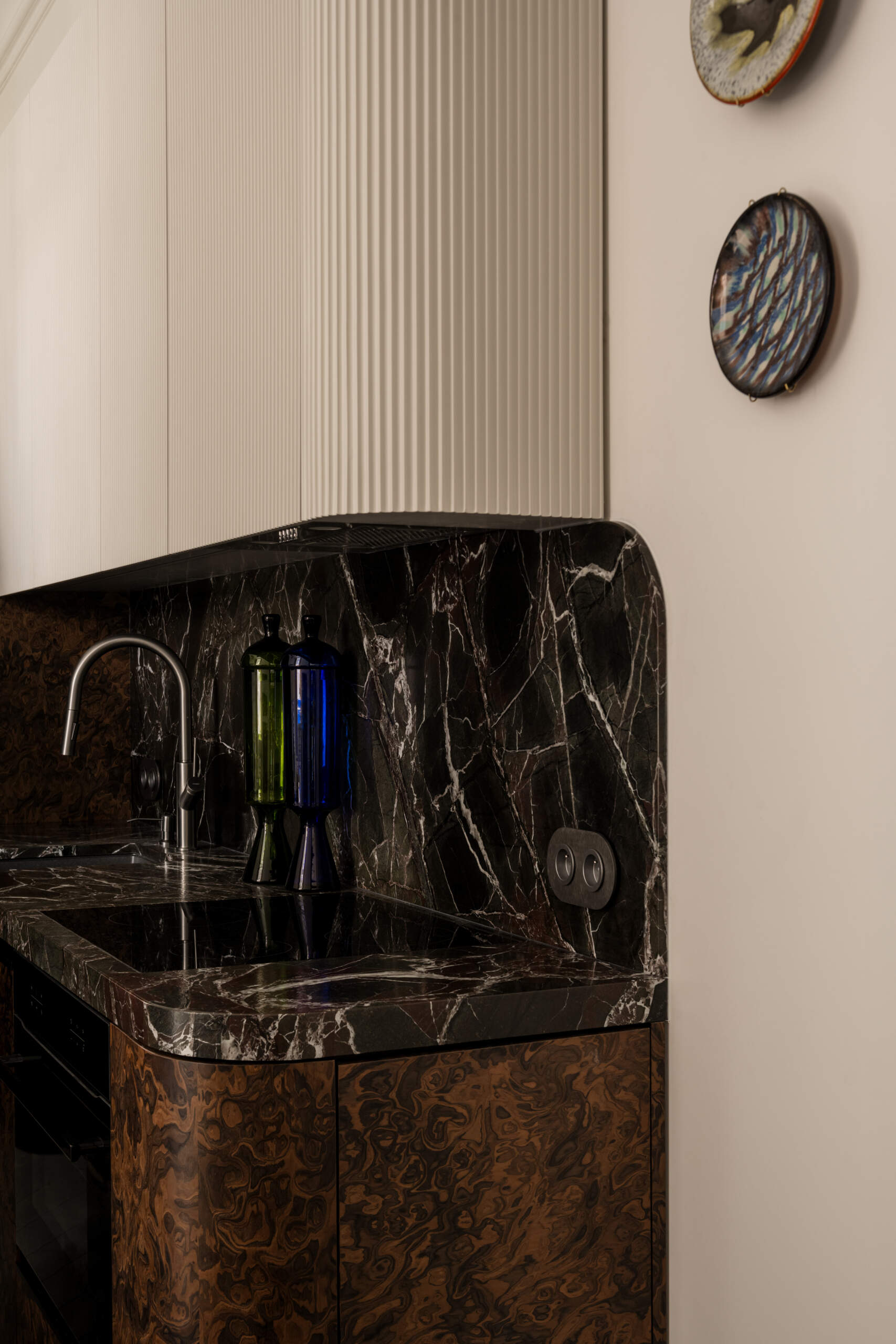 In the kitchen, a deep green Rosso Levanto marble meets California Burl veneer for a dramatic contrast. A burst of Chinese red inside the cabinets adds surprise, while a glossy ultramarine console defines the open-plan living area with bold color and precision.