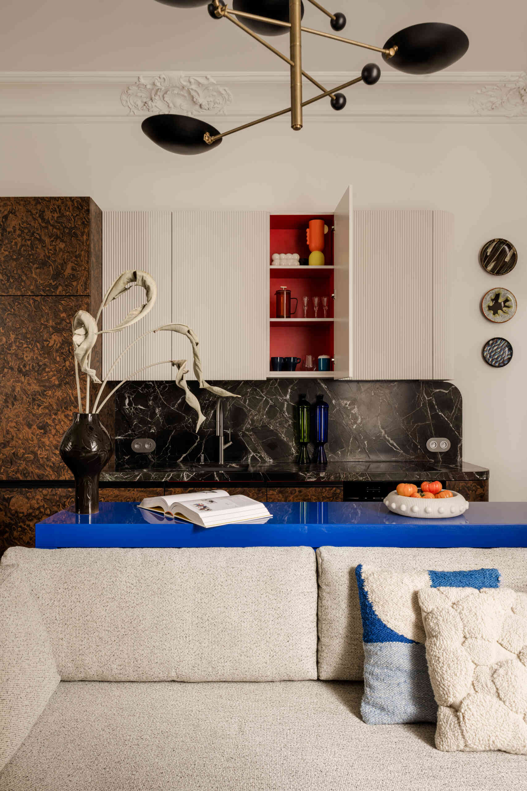 In the kitchen, a deep green Rosso Levanto marble meets California Burl veneer for a dramatic contrast. A burst of Chinese red inside the cabinets adds surprise, while a glossy ultramarine console defines the open-plan living area with bold color and precision.