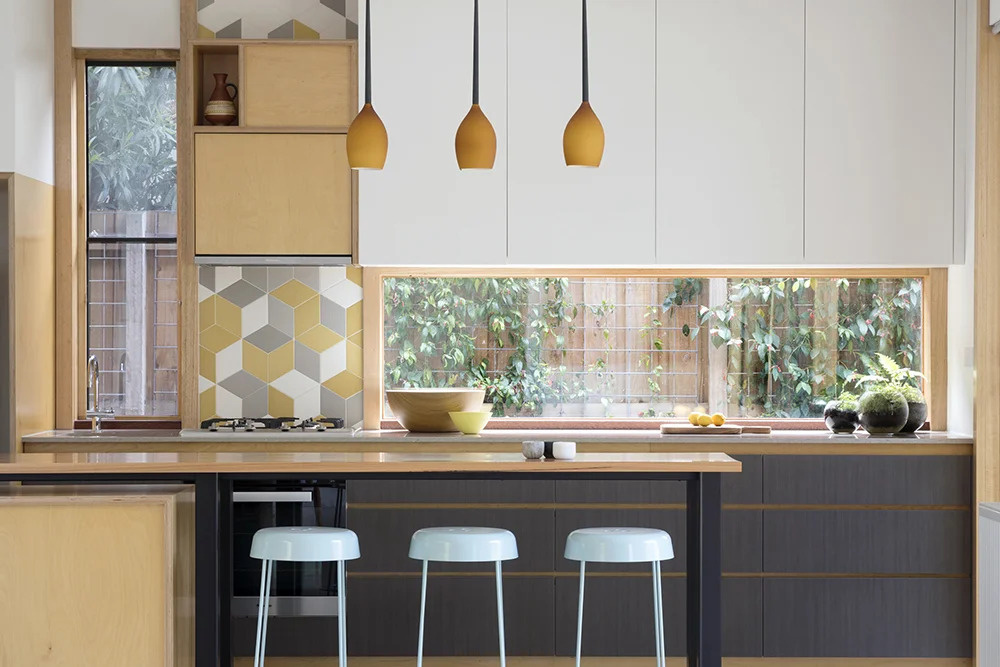 A bright, modern kitchen where windows double as backsplashes and a hint of color adds cheerful personality.