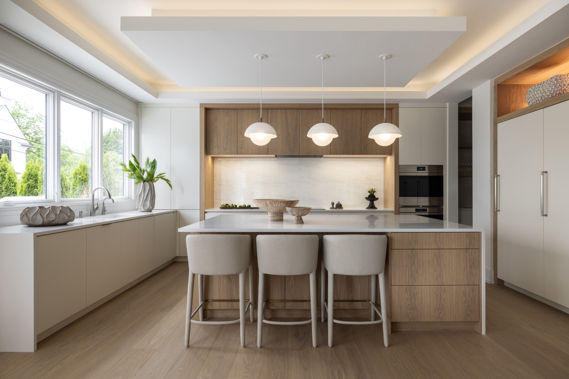 In the kitchen, wood and white do the talking. Three sculptural globe pendants hover above a generous island, while quiet cabinetry keeps the visual noise to a minimum. The palette is restrained, the textures do the lifting, and the result is exactly what busy mornings need. Practical yet polished. Appliances tuck away. Traffic flows. The whole space feels calm and collected.
