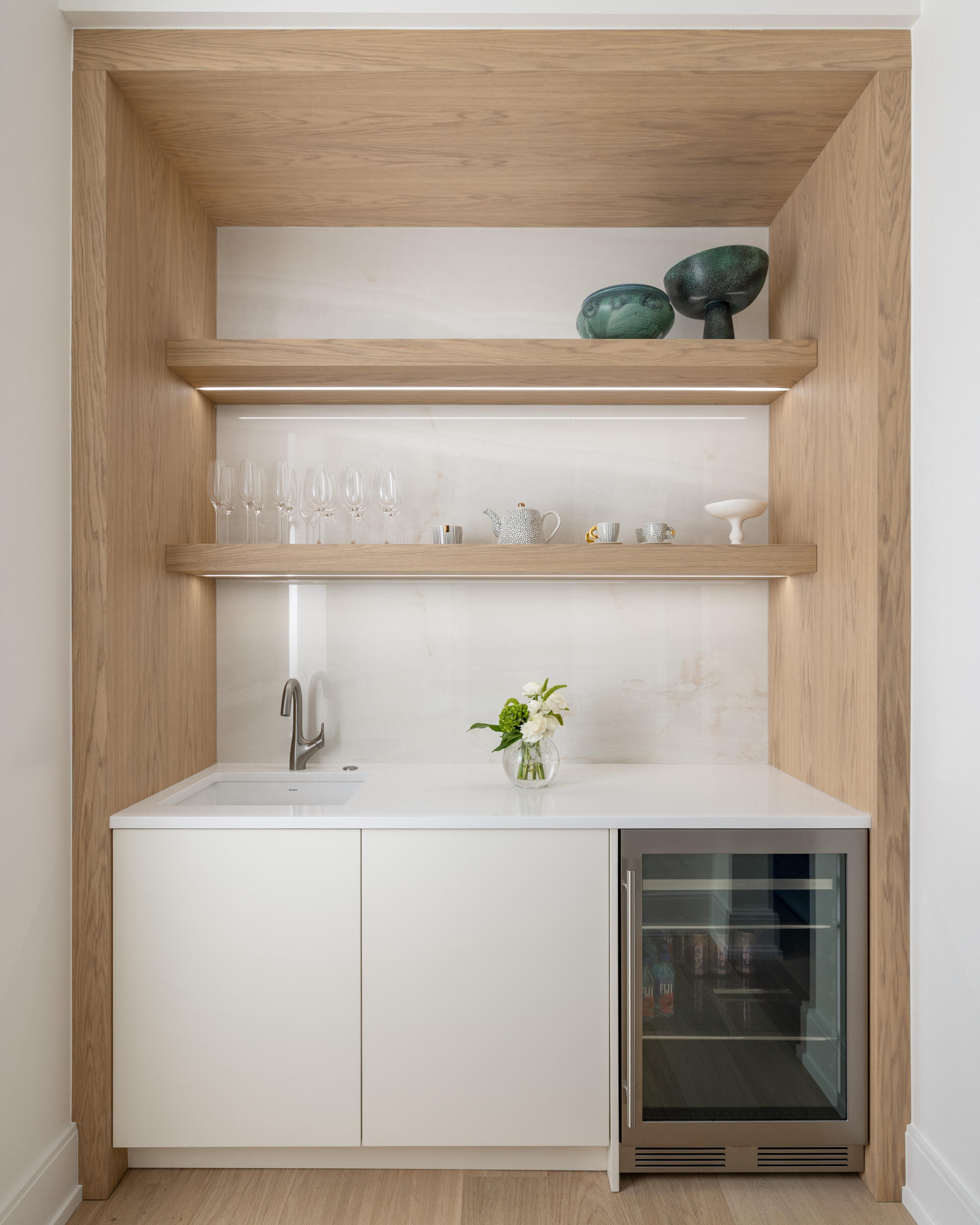 In the kitchen, wood and white do the talking. Three sculptural globe pendants hover above a generous island, while quiet cabinetry keeps the visual noise to a minimum. The palette is restrained, the textures do the lifting, and the result is exactly what busy mornings need. Practical yet polished. Appliances tuck away. Traffic flows. The whole space feels calm and collected.