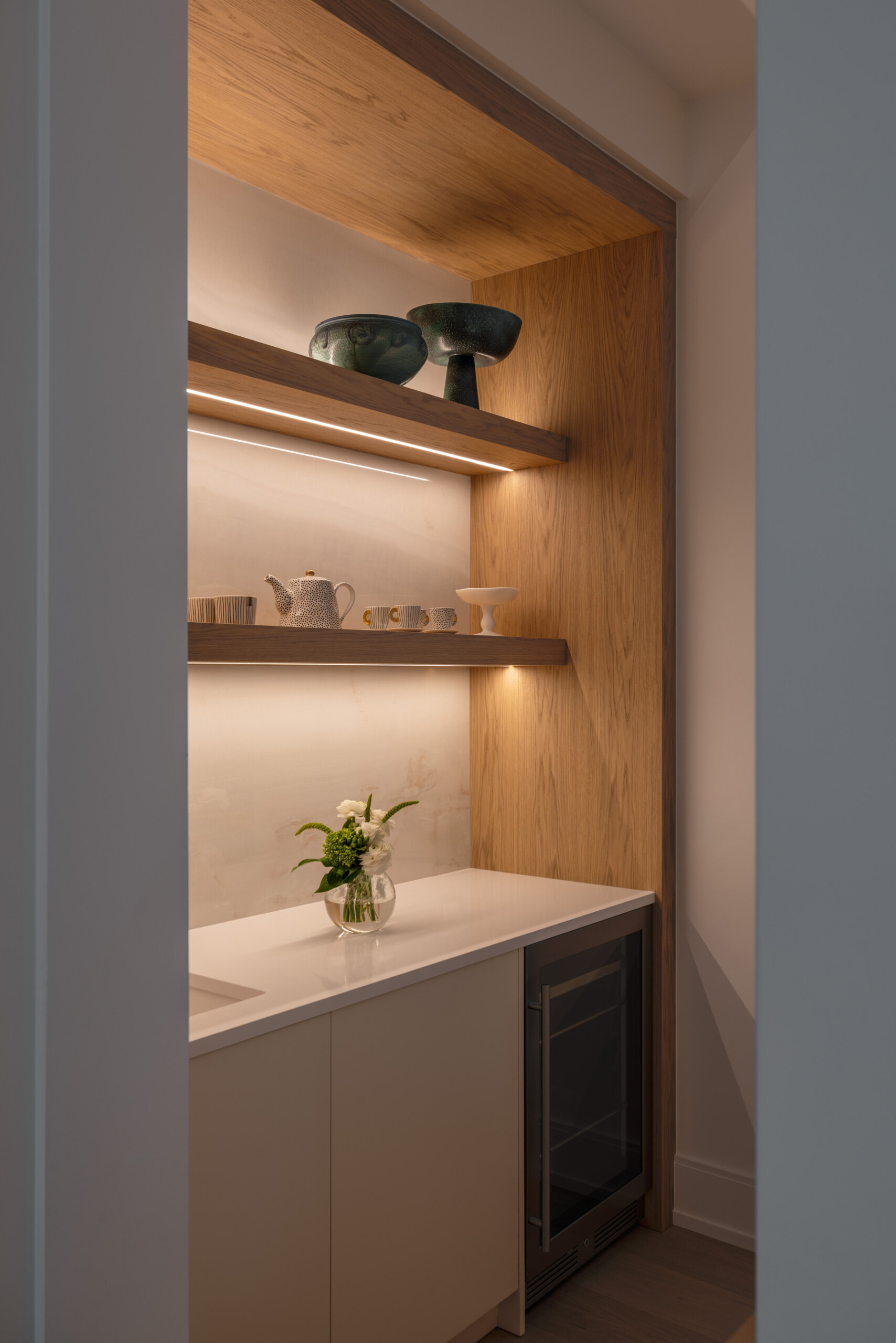 In the kitchen, wood and white do the talking. Three sculptural globe pendants hover above a generous island, while quiet cabinetry keeps the visual noise to a minimum. The palette is restrained, the textures do the lifting, and the result is exactly what busy mornings need. Practical yet polished. Appliances tuck away. Traffic flows. The whole space feels calm and collected.