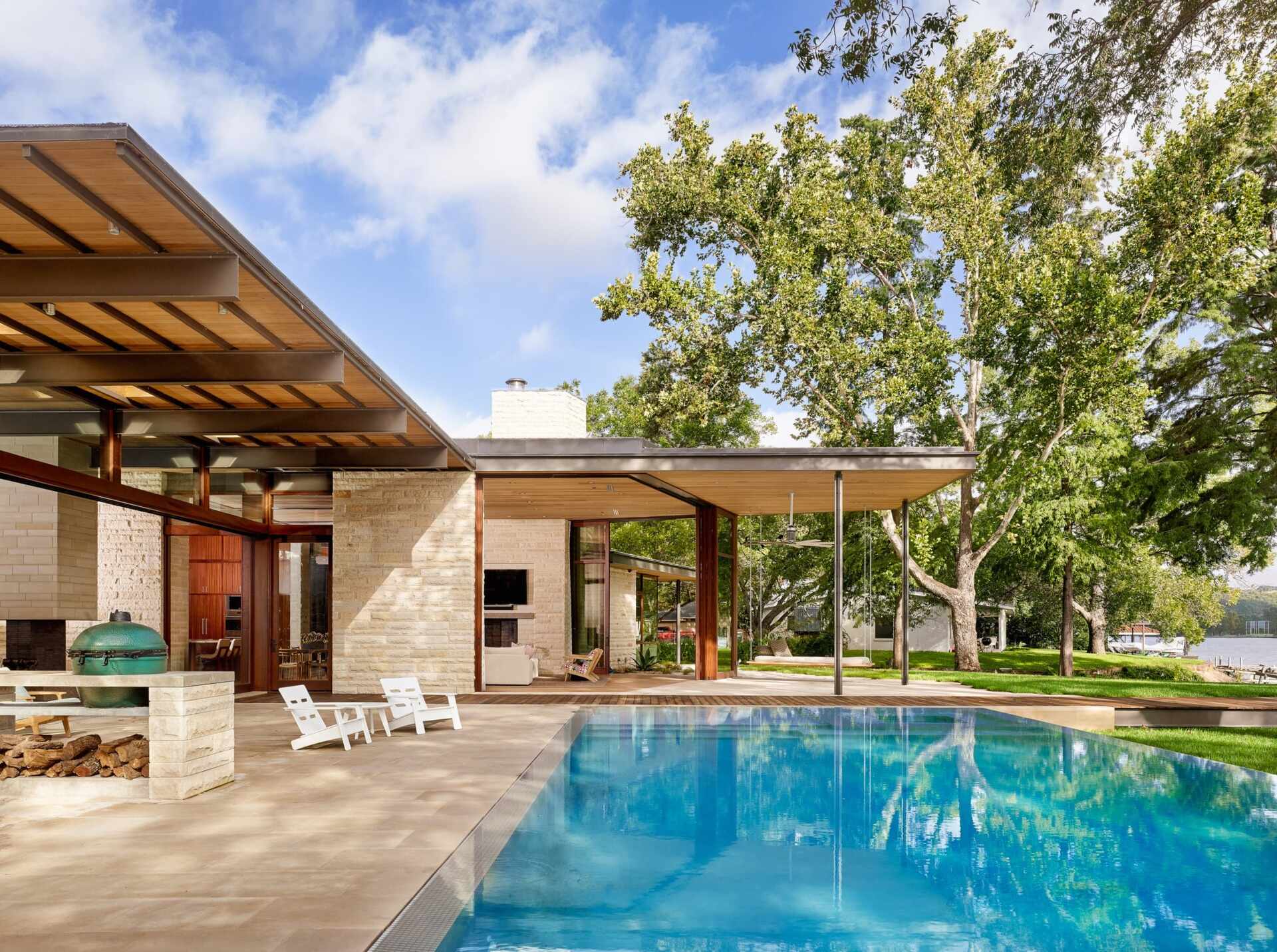 A covered deck and shimmering pool extend toward the lake, merging shade, sunlight, and water in one perfect outdoor retreat.