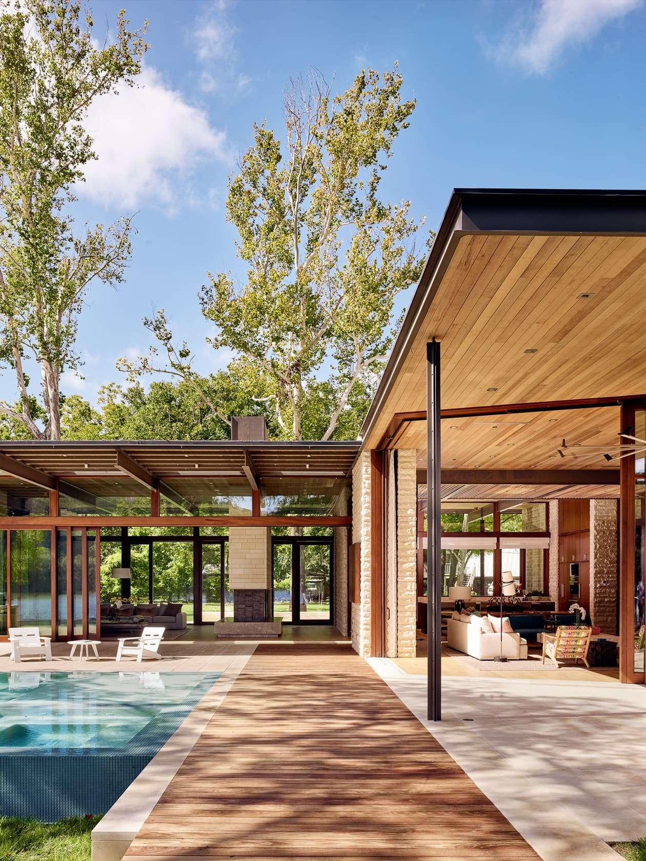 A covered deck and shimmering pool extend toward the lake, merging shade, sunlight, and water in one perfect outdoor retreat.