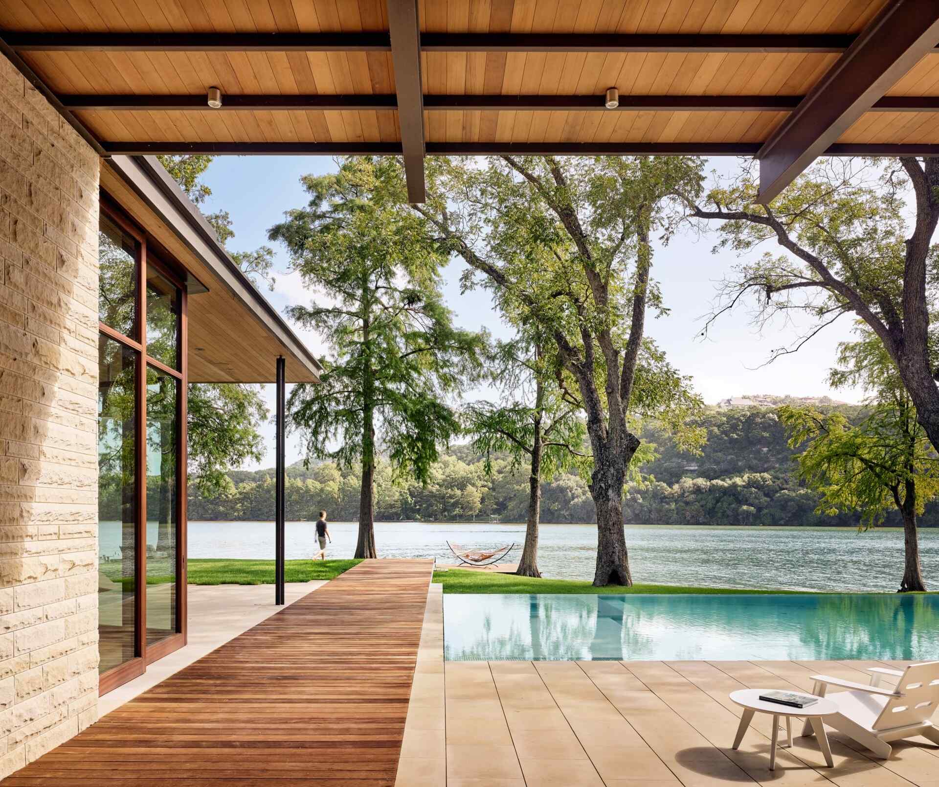 A covered deck and shimmering pool extend toward the lake, merging shade, sunlight, and water in one perfect outdoor retreat.
