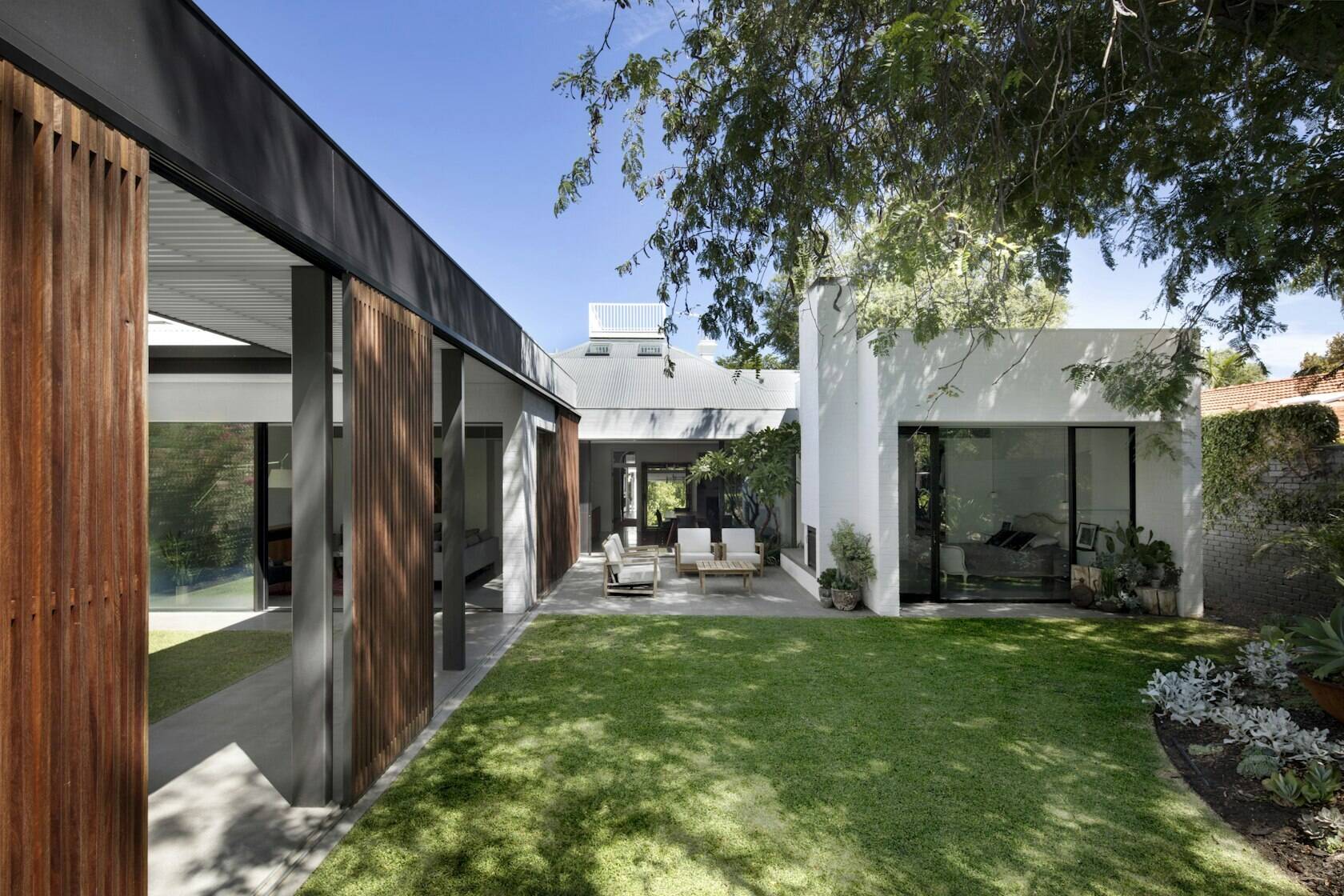 A refined modern house extension  with white brick volumes and dark steel and wood accents surrounded by lush gardens.