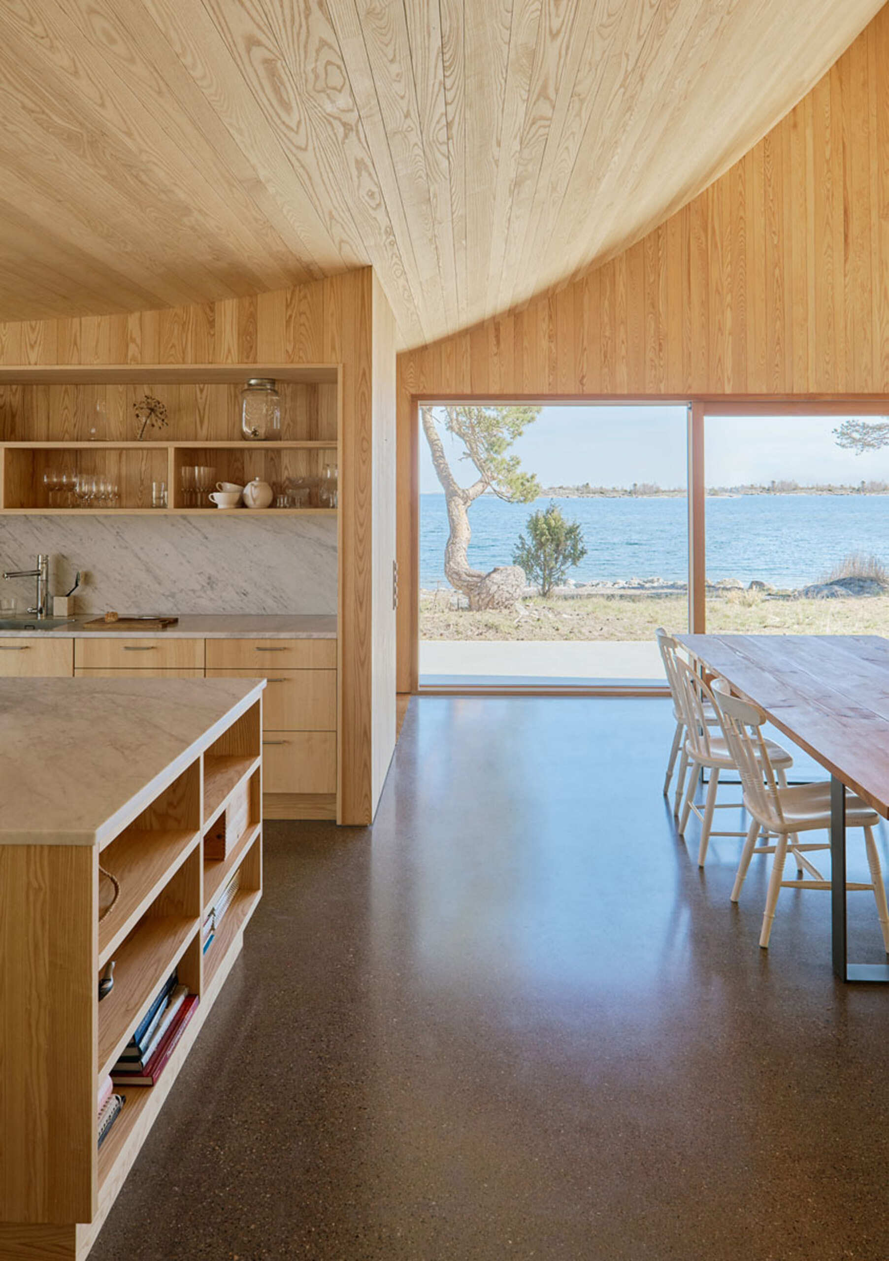 Soft wood tones and a simple grey counter define this airy kitchen, which opens to a private terrace with views of pine and sea.