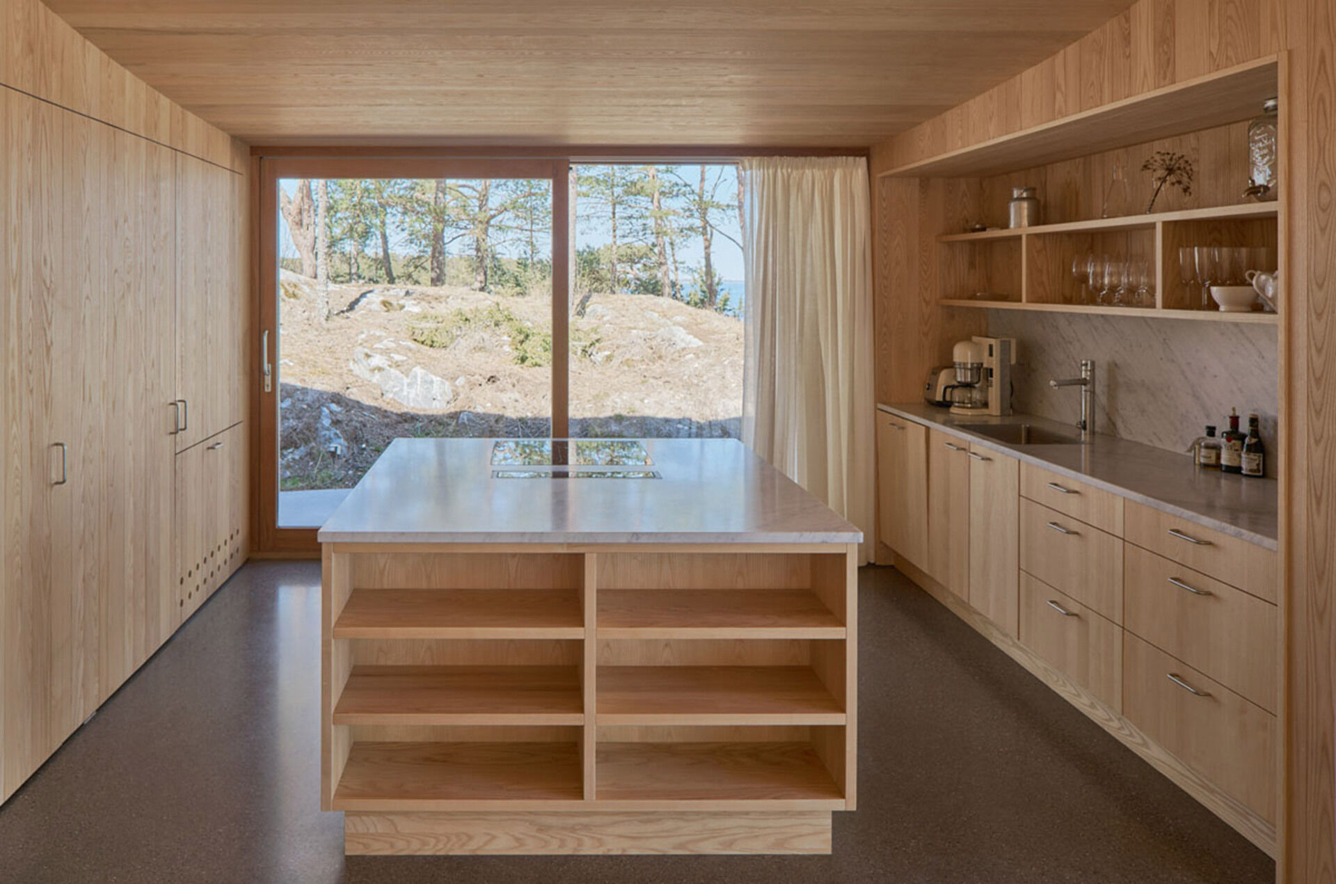 Soft wood tones and a simple grey counter define this airy kitchen, which opens to a private terrace with views of pine and sea.