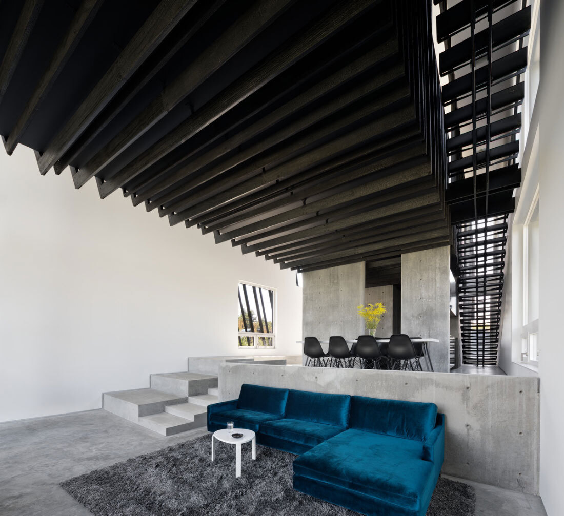 A bright blue couch and panoramic mountain views bring life and warmth to this minimalist living room framed by concrete and glass.