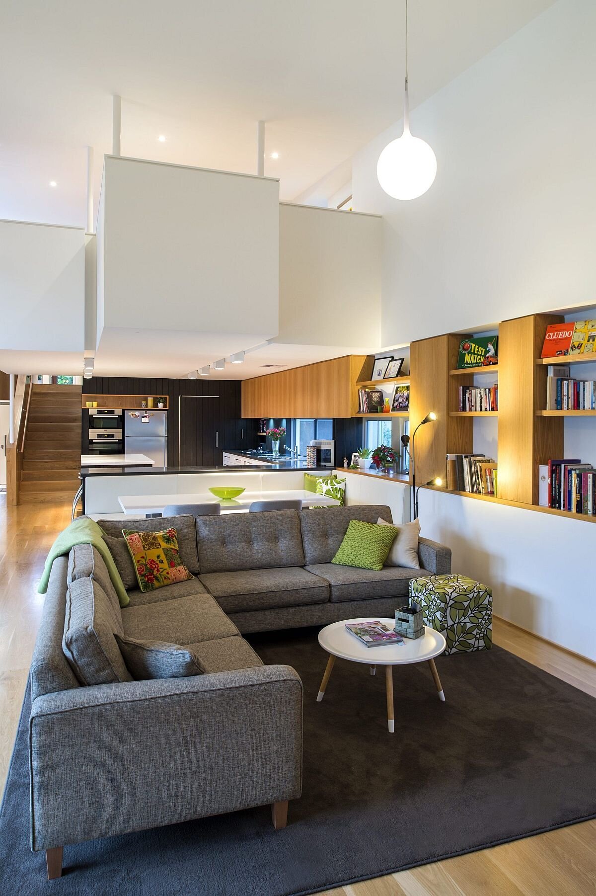 Timber shelving and cabinetry add warmth to the informal living area, leading into the kitchen. A black accent wall and timber shelf give the kitchen a simple, mid-century character.
