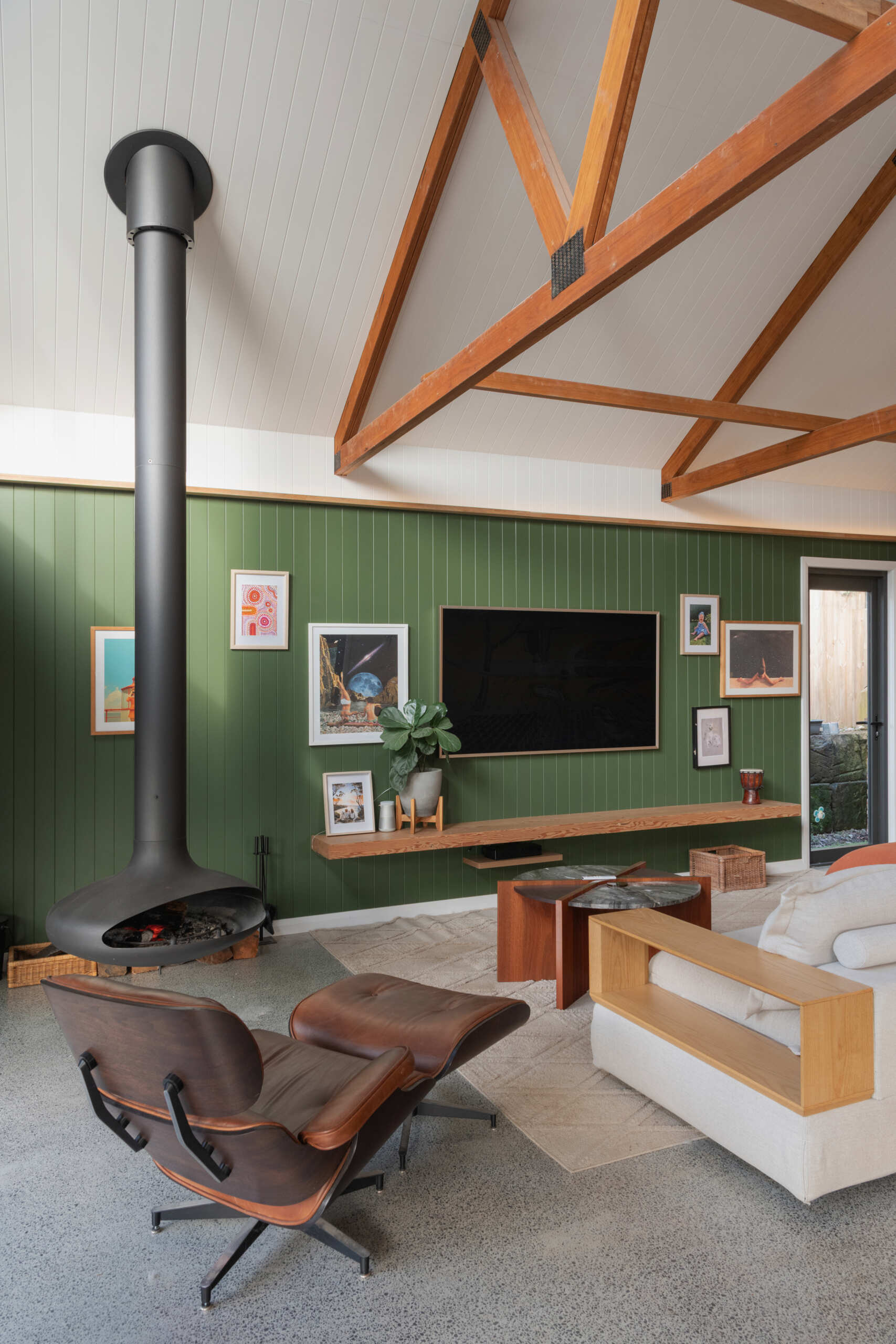 The open-plan living space centers around a floating fireplace and soft green feature wall. Built-in cabinetry conceals storage, a bar, and a desk, giving the room both warmth and quiet order.