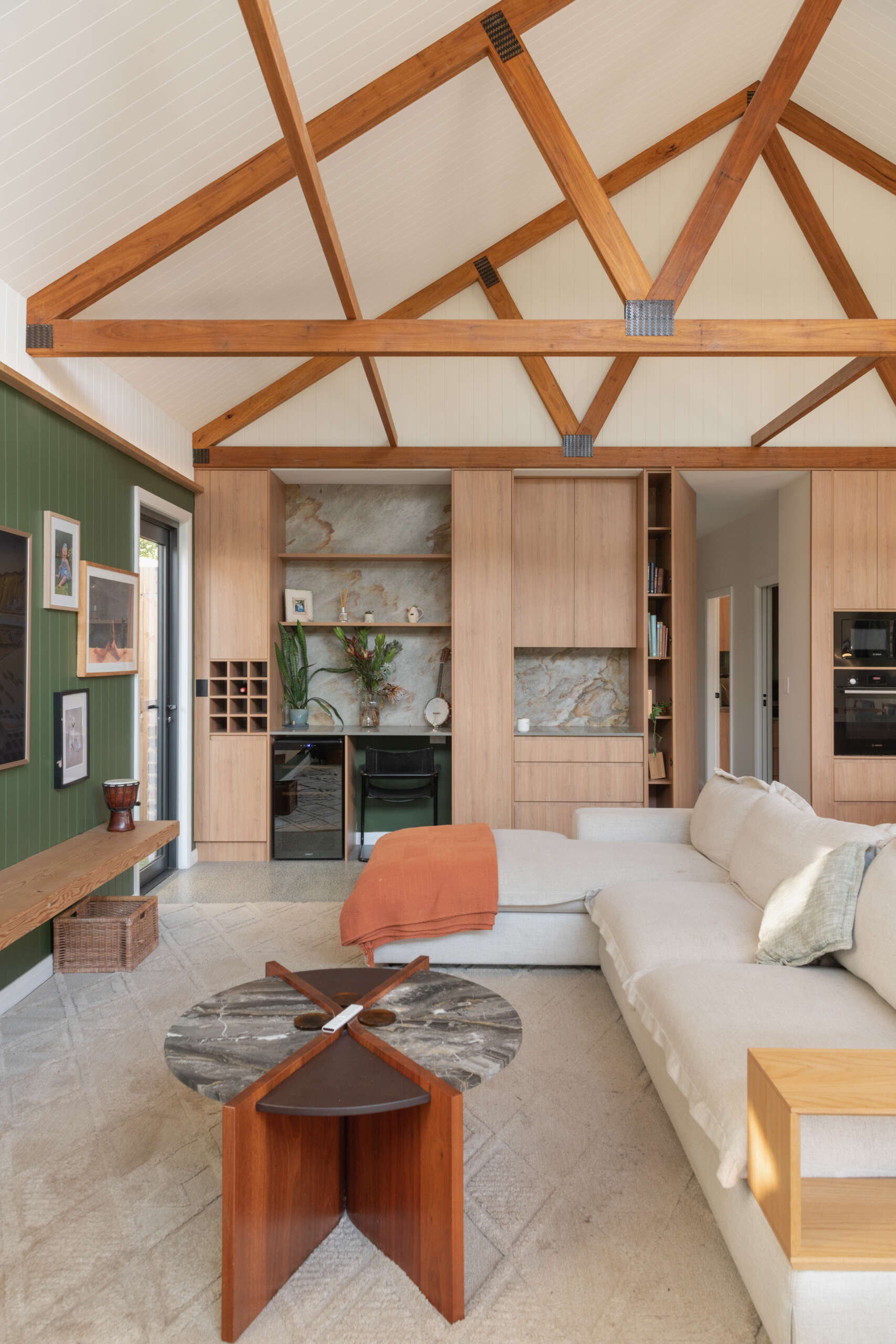 The open-plan living space centers around a floating fireplace and soft green feature wall. Built-in cabinetry conceals storage, a bar, and a desk, giving the room both warmth and quiet order.