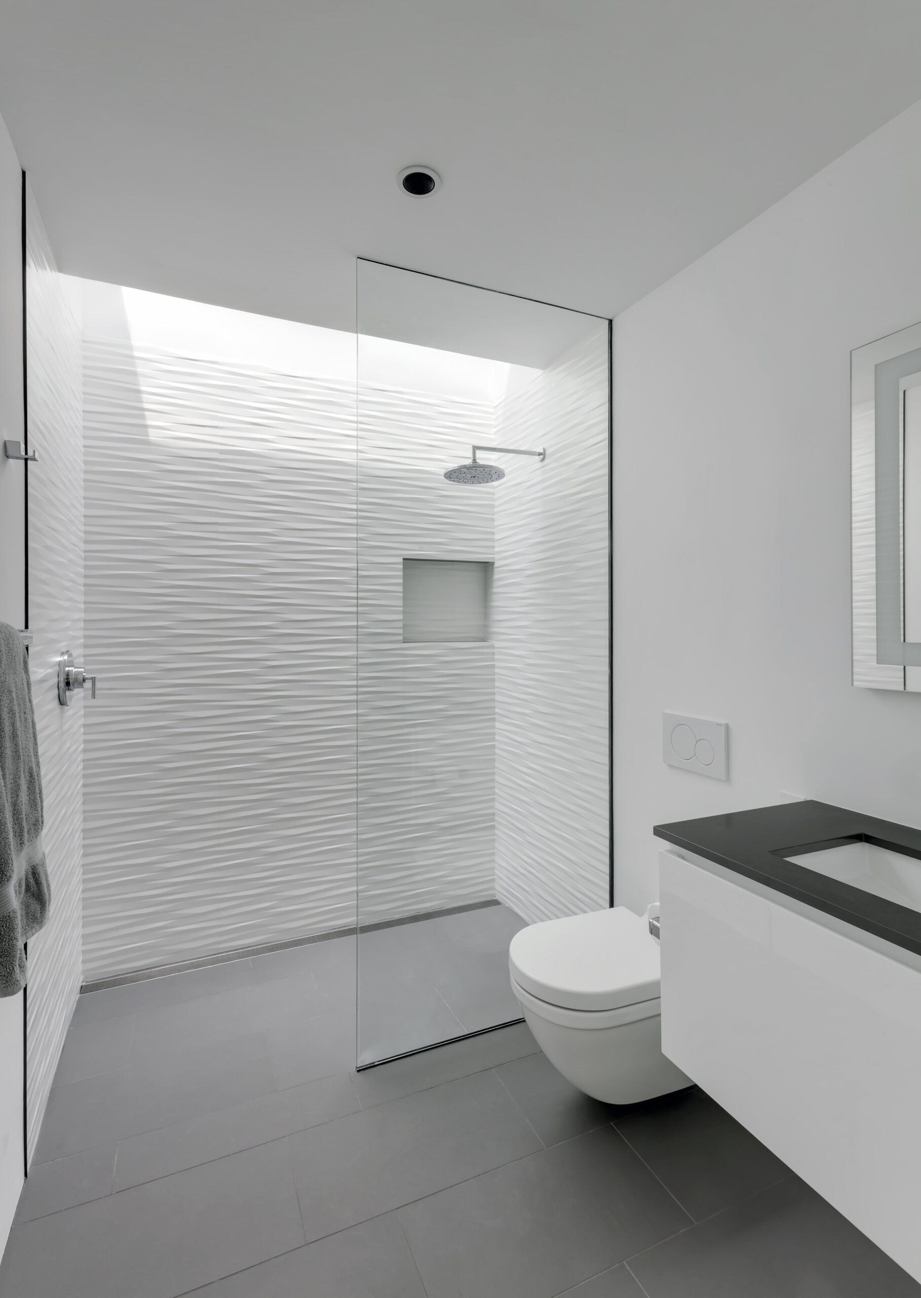 In this bathroom there's a blend of grey floor tiles and textured white walls, all lit by a skylight that brings daylight directly into the shower.