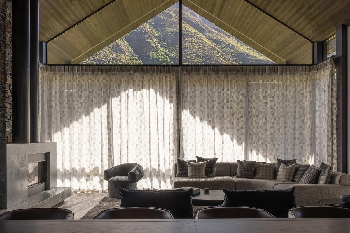 Soaring gable ceilings and expansive glazing flood the living room with natural light. Every angle has been considered to maximize the connection between indoors and the alpine panorama. The openness feels balanced by the grounding effect of the stone walls, giving the room both drama and warmth.