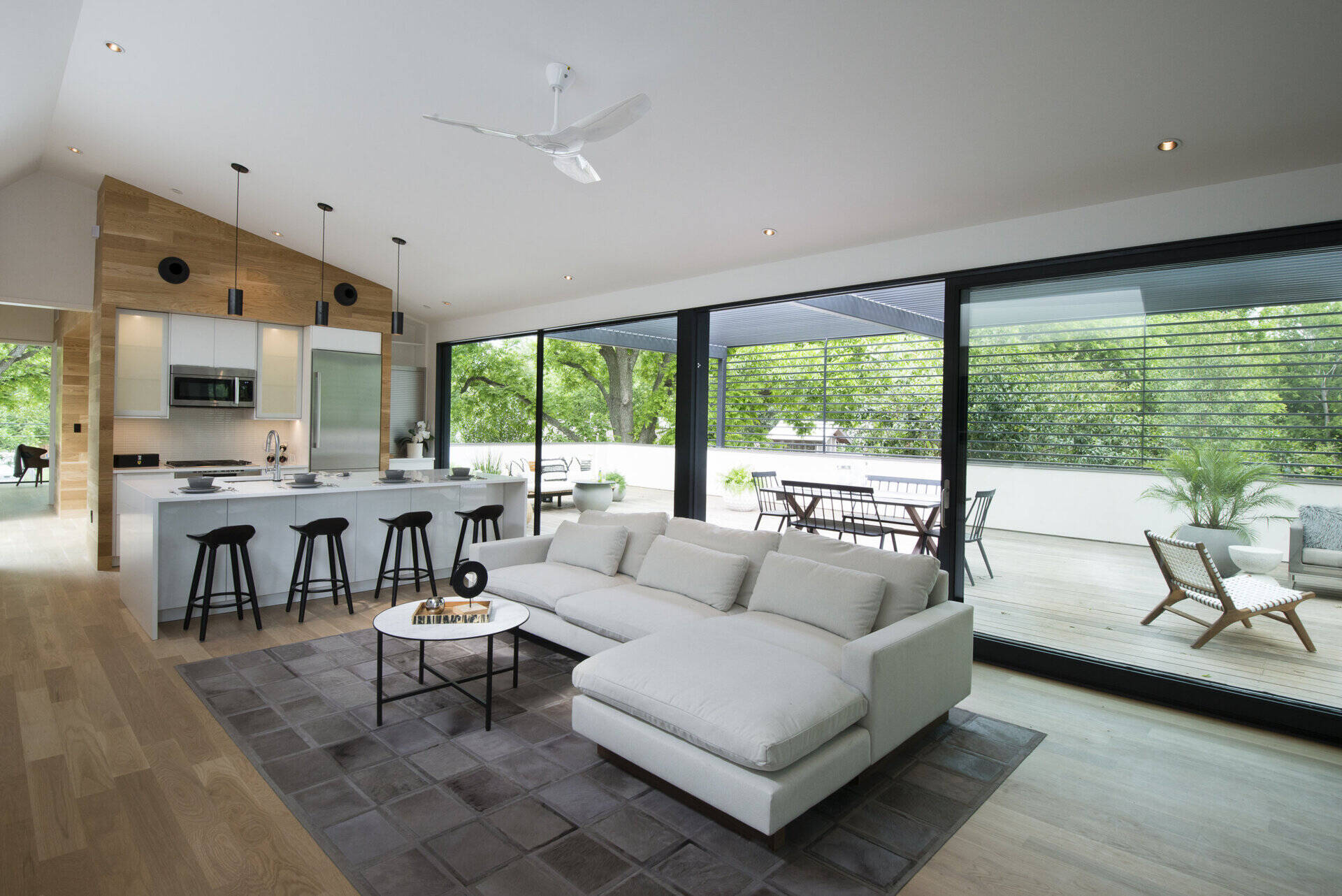 The living room and kitchen share one airy space, softened by wood flooring and a warm accent wall that balance the clean white surfaces.